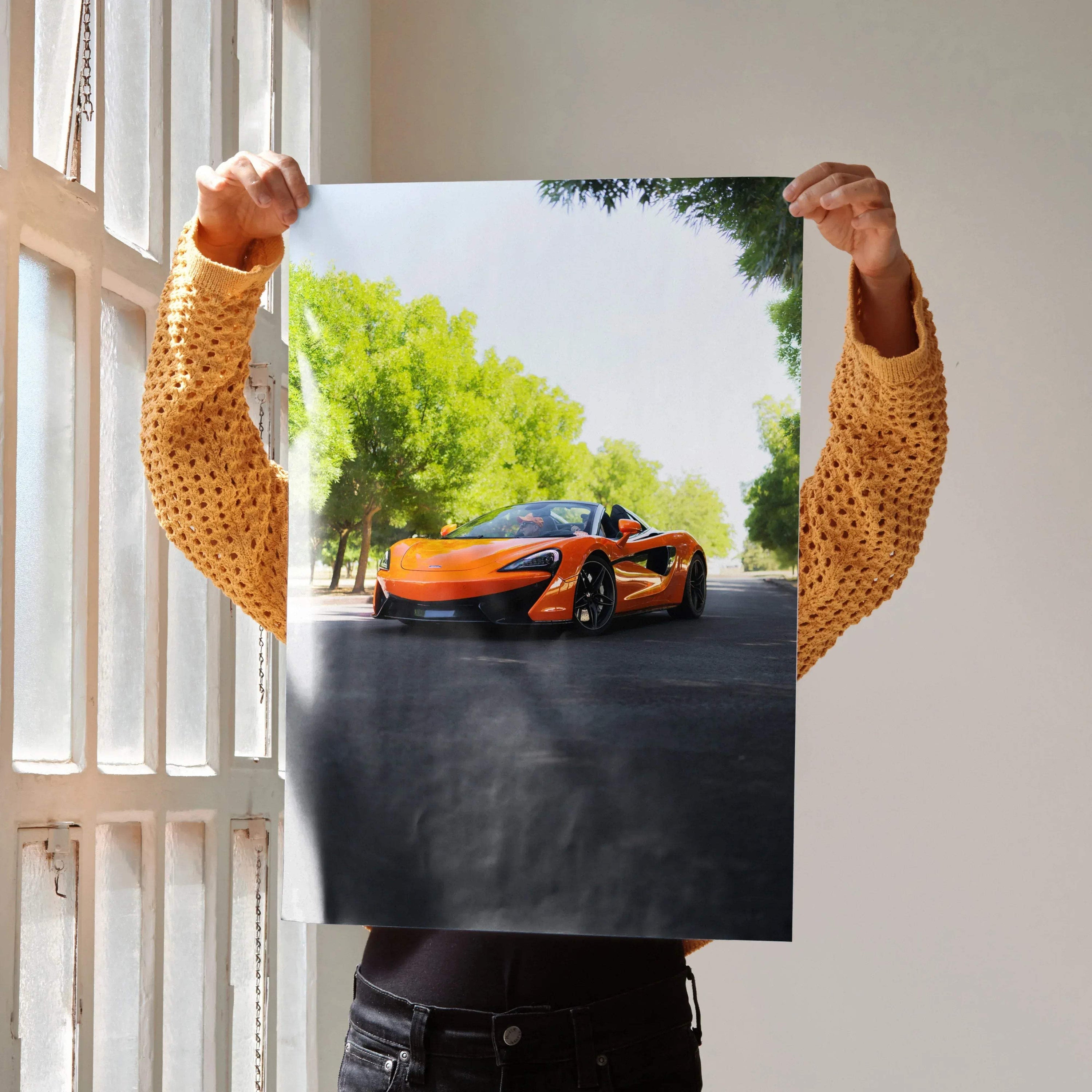 McLaren 570S orange sports car poster wall art held by person near window.