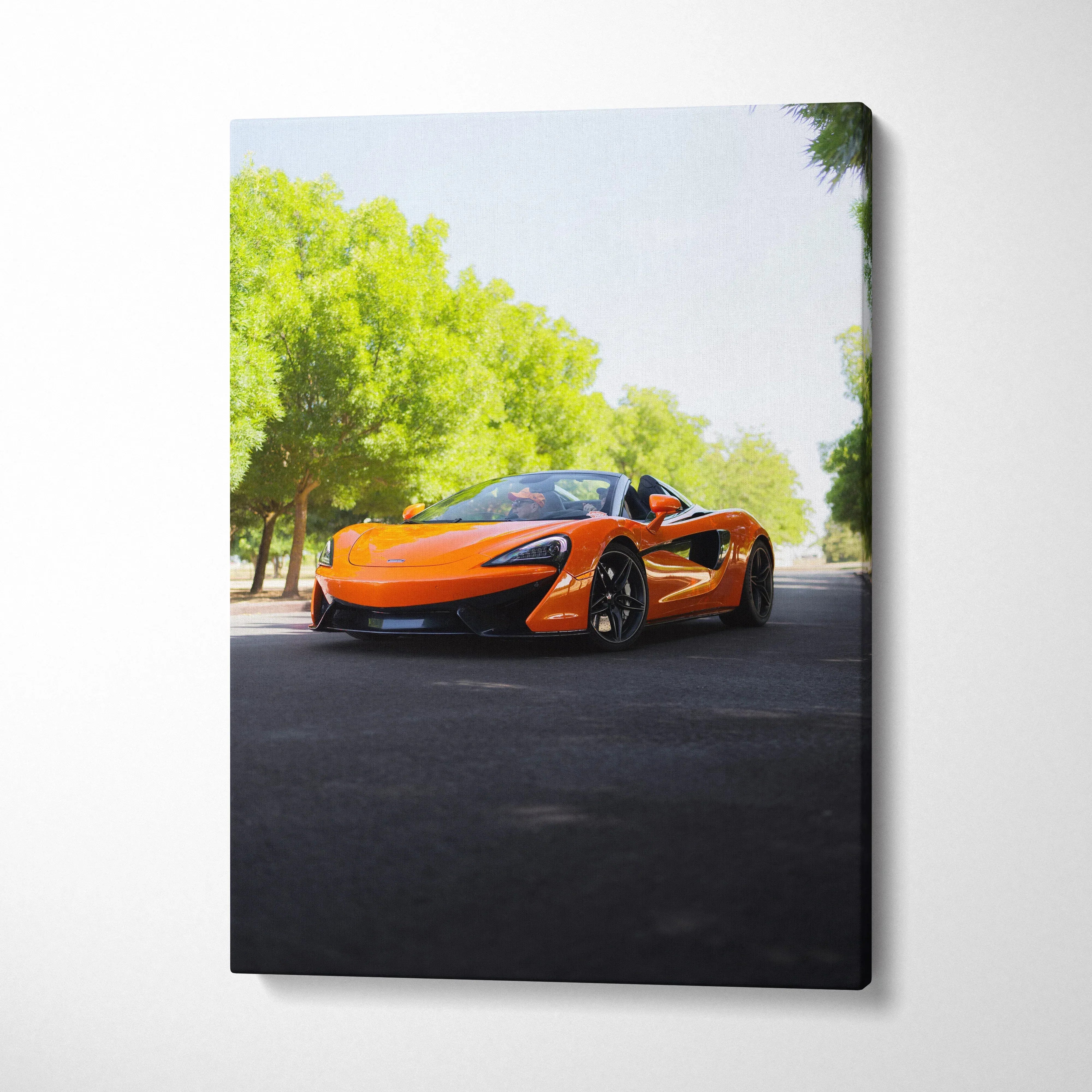 Orange McLaren 570S sports car on road surrounded by green trees vertical canvas wall art.