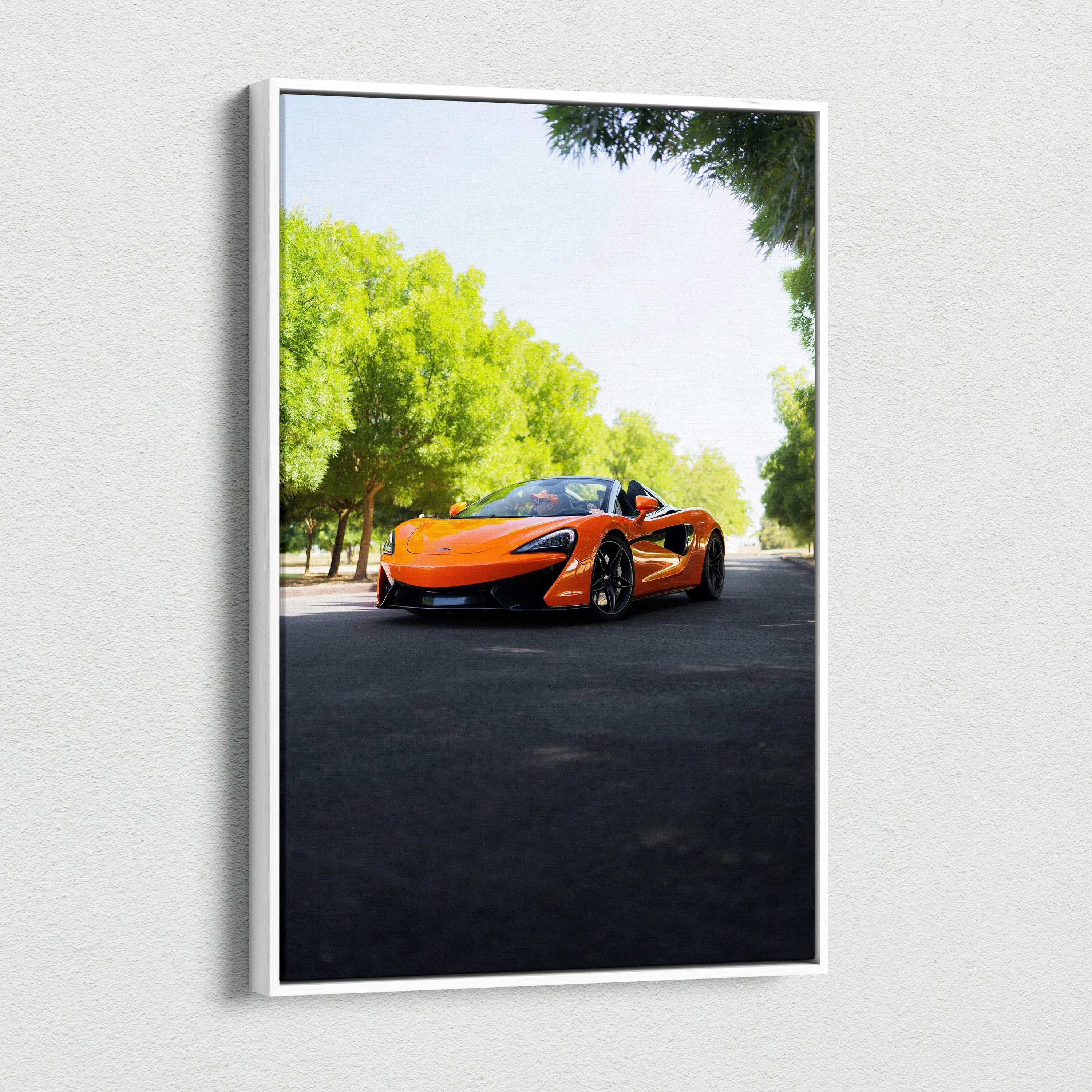 Vertical canvas wall art featuring an orange McLaren 570S sports car on a sunlit road with green trees.