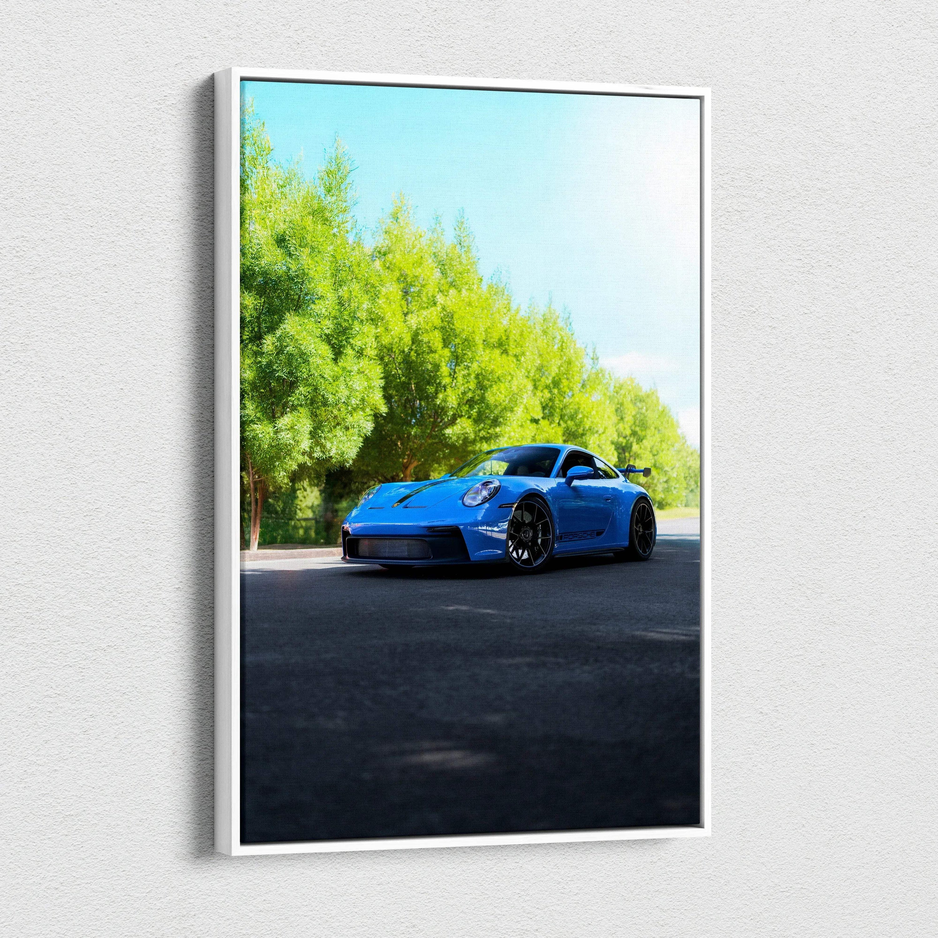 Vertical canvas wall art featuring a blue Porsche 911 GT3 parked on sunlit asphalt beside green trees.