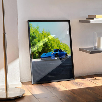 Porsche 911 GT3 racing car poster with vivid green trees background, framed wall art leaning on floor.