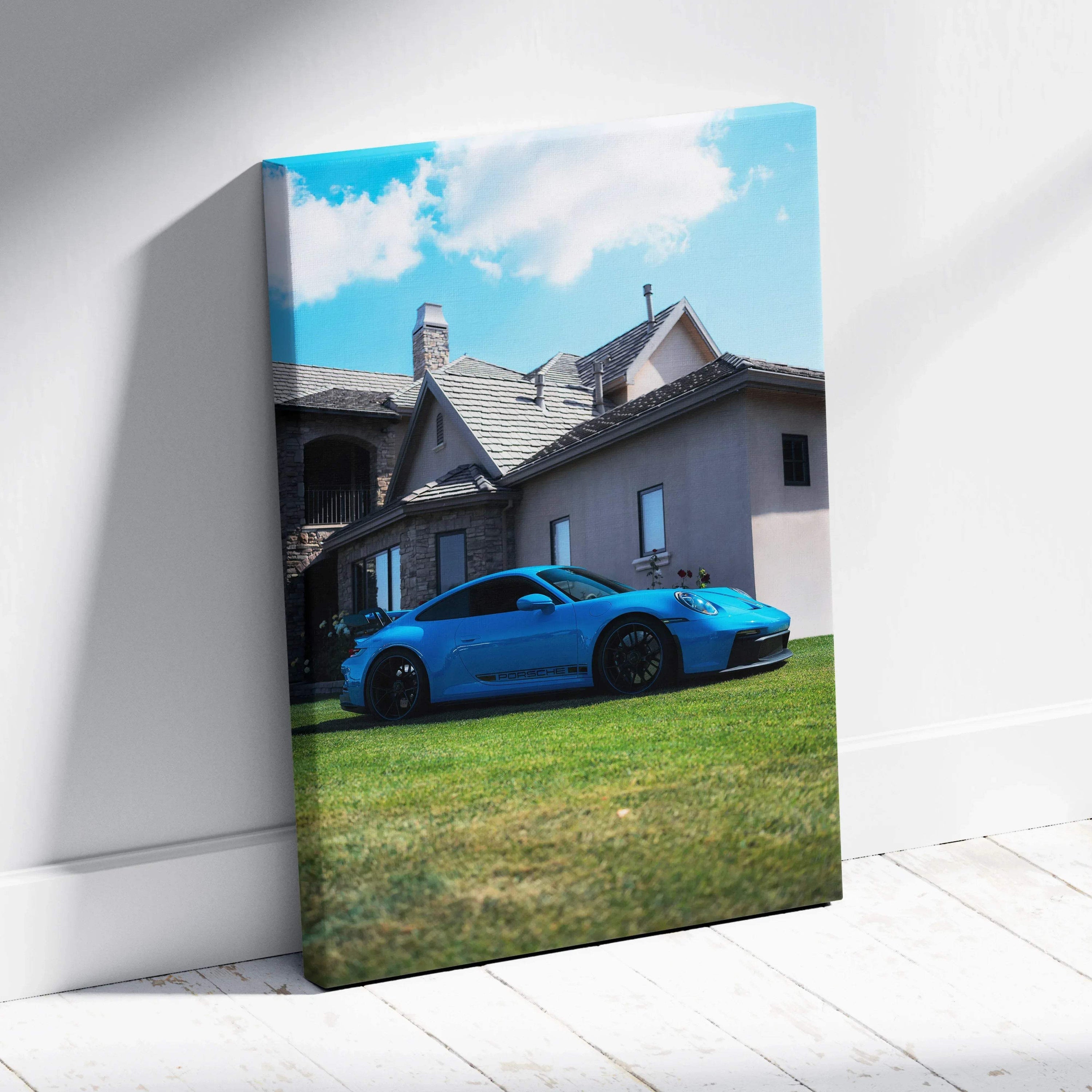 Vertical canvas wall art featuring a blue Porsche 911 GT3 parked on grass in front of a house under a blue sky.
