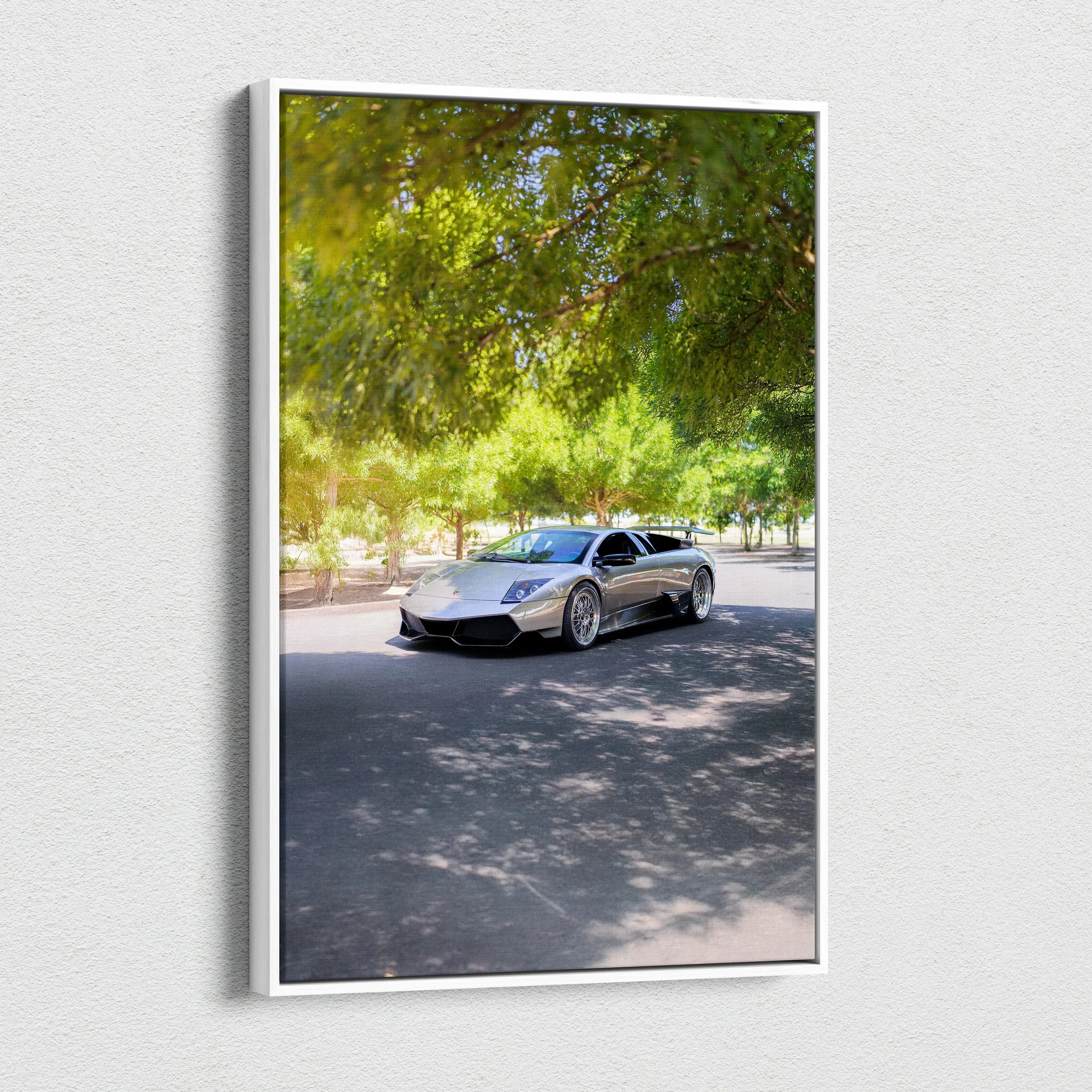 Vertical canvas wall art featuring a silver Lamborghini Murcielago under green leafy trees.