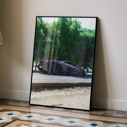 Lamborghini Revuelto poster with sleek black sports car and lush green trees as wall art in black frame.