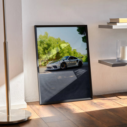 Porsche 911 GT3 poster with black frame leaning against wall, vibrant car and trees in background, modern wall art.