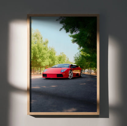 Red Lamborghini Murcielago parked under green trees, sleek car poster wall art in wooden frame.
