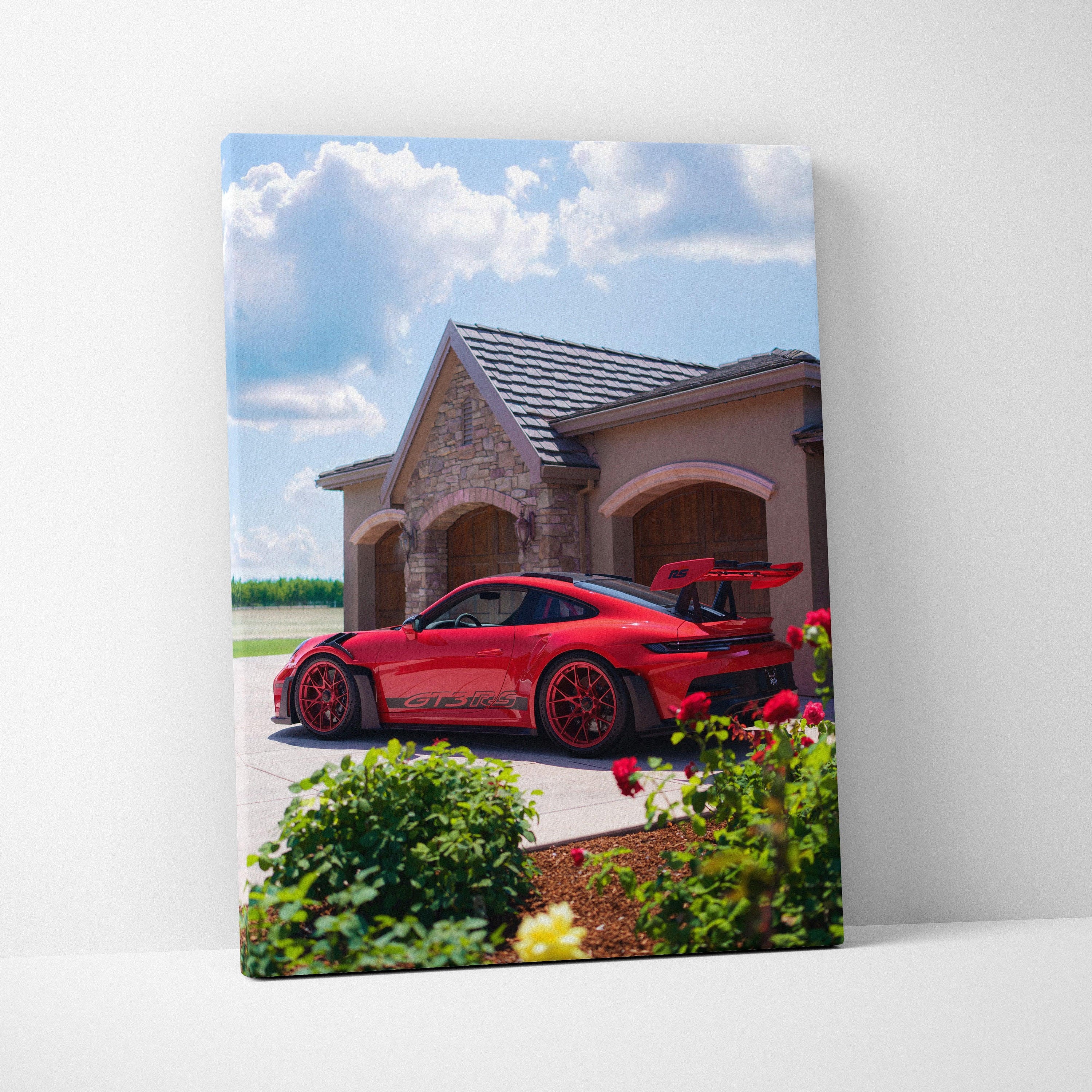 Vertical canvas art featuring a red Porsche 911 GT3 RS parked outside a stone house under a bright sky.