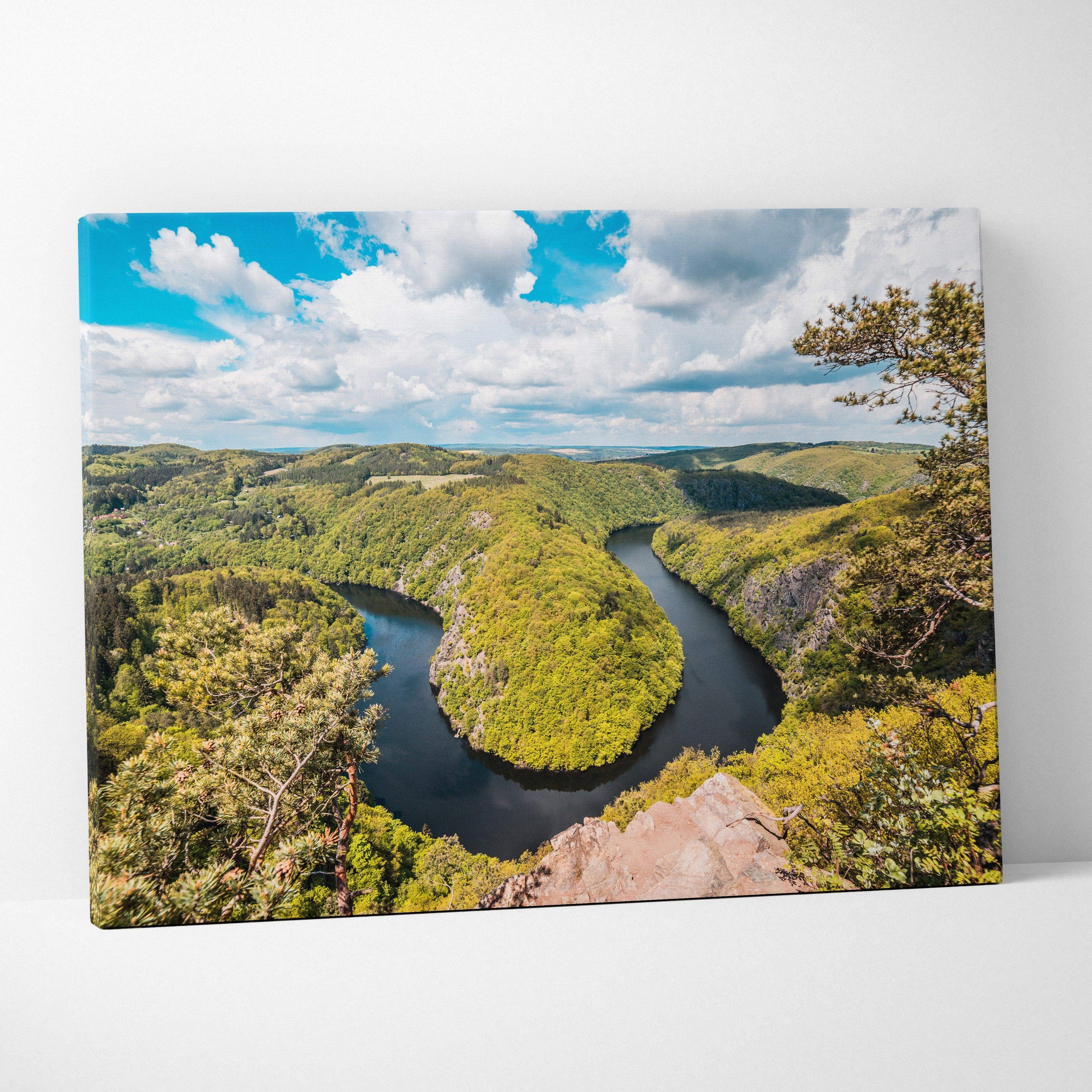 Canvas print of meandering river through lush green forest valleys under blue sky