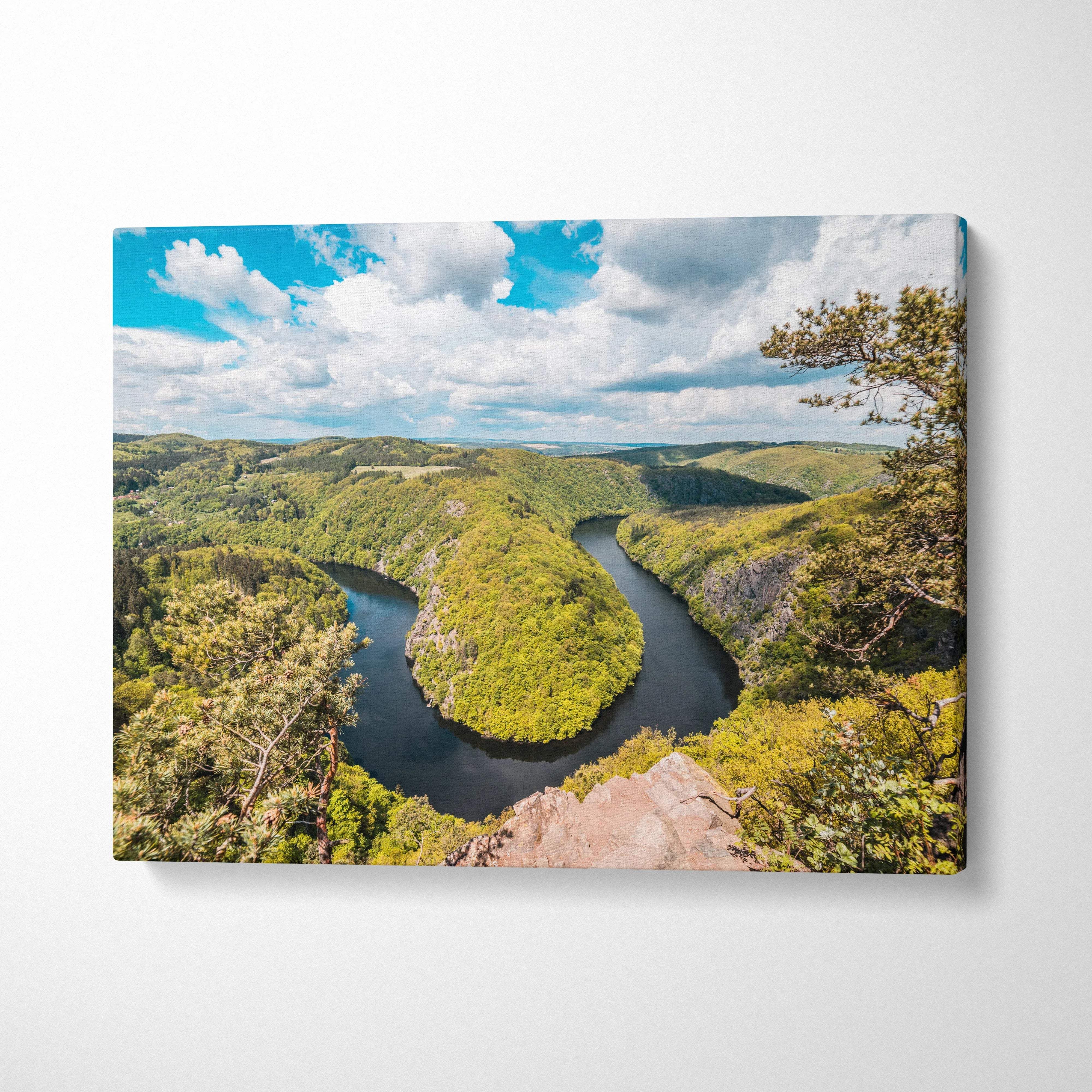 Canvas print of meandering river through lush green forest valleys under blue sky
