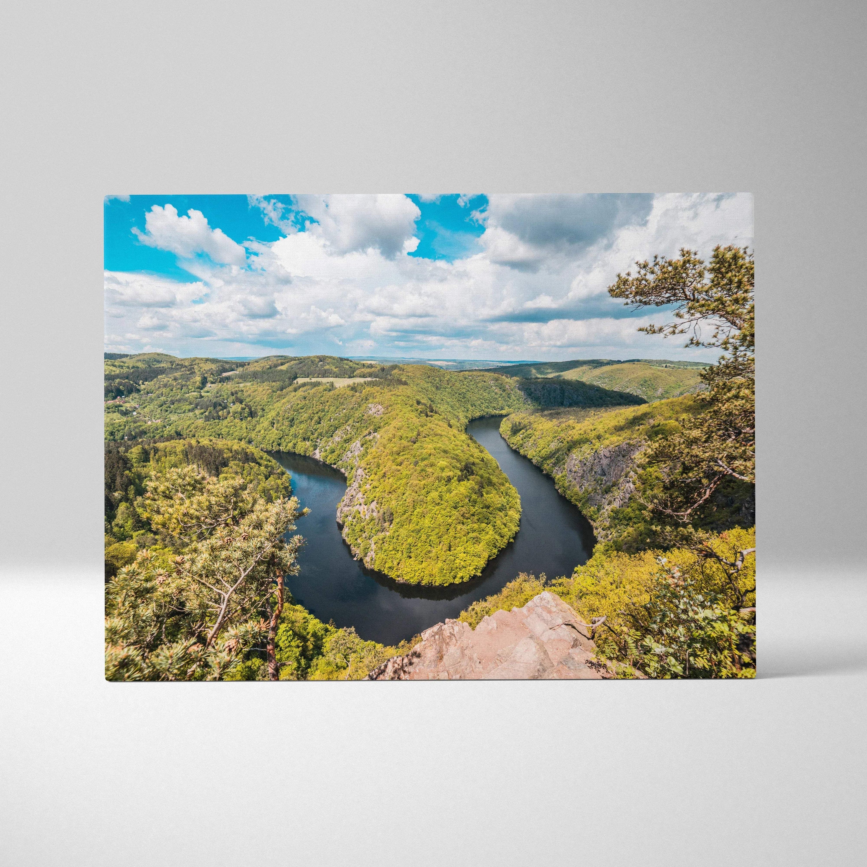 Canvas print of meandering river through lush green forest valleys under blue sky