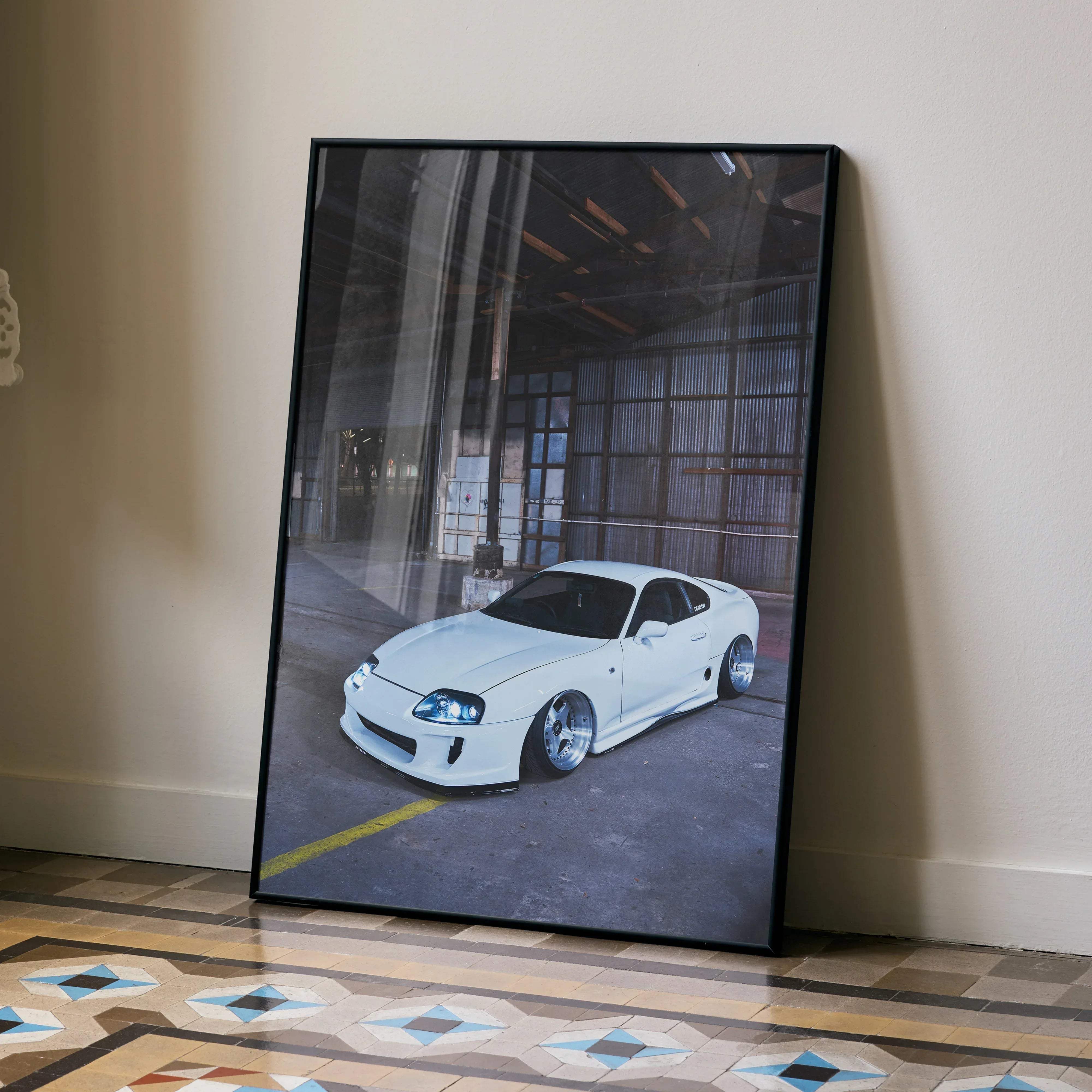 A framed black-and-white photograph of a white Toyota Supra sports car in an industrial garage wall decor print