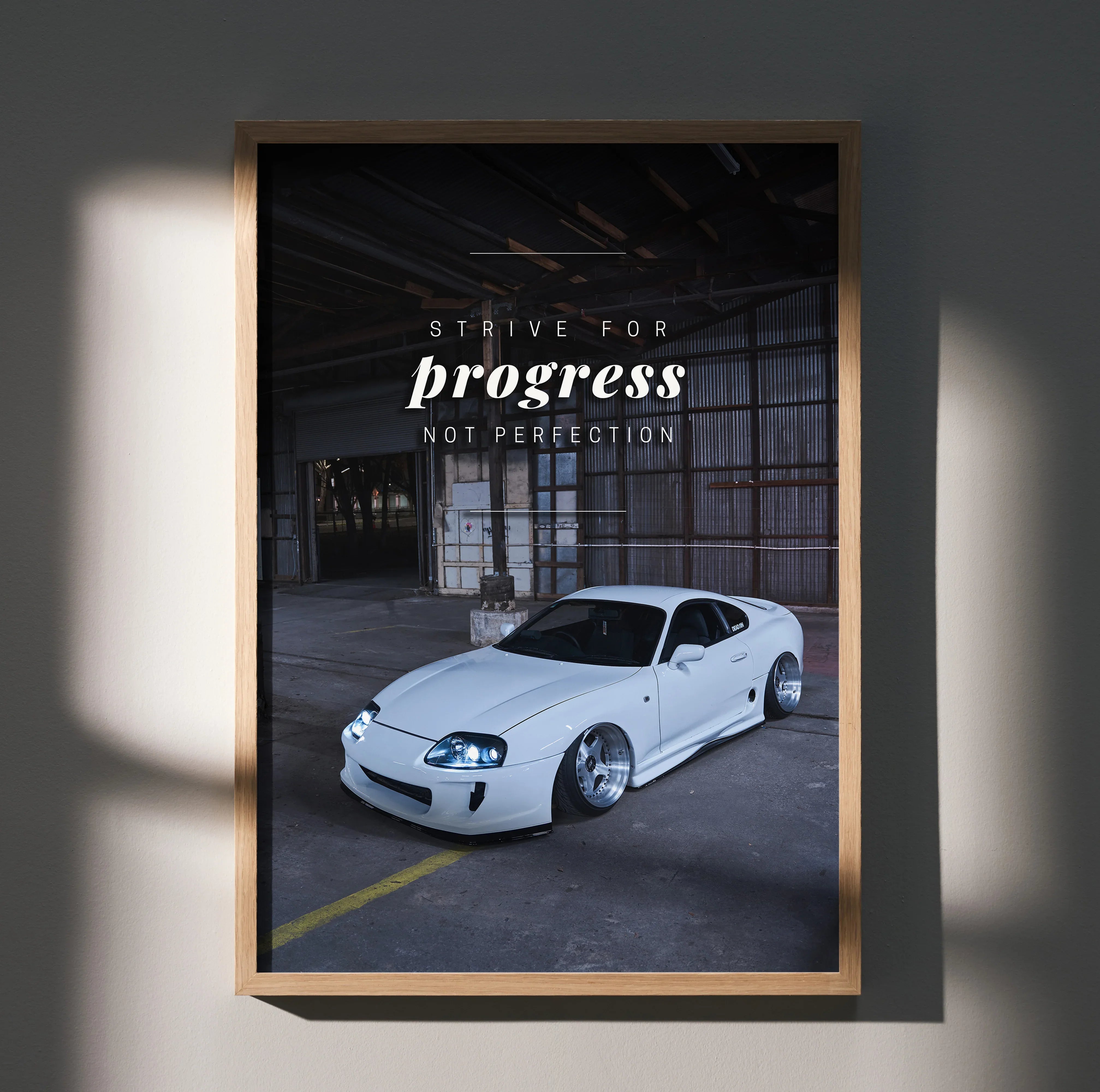 Motivational poster wall art featuring a white Toyota Supra Mk4 inside an industrial garage with "Strive for progress not.