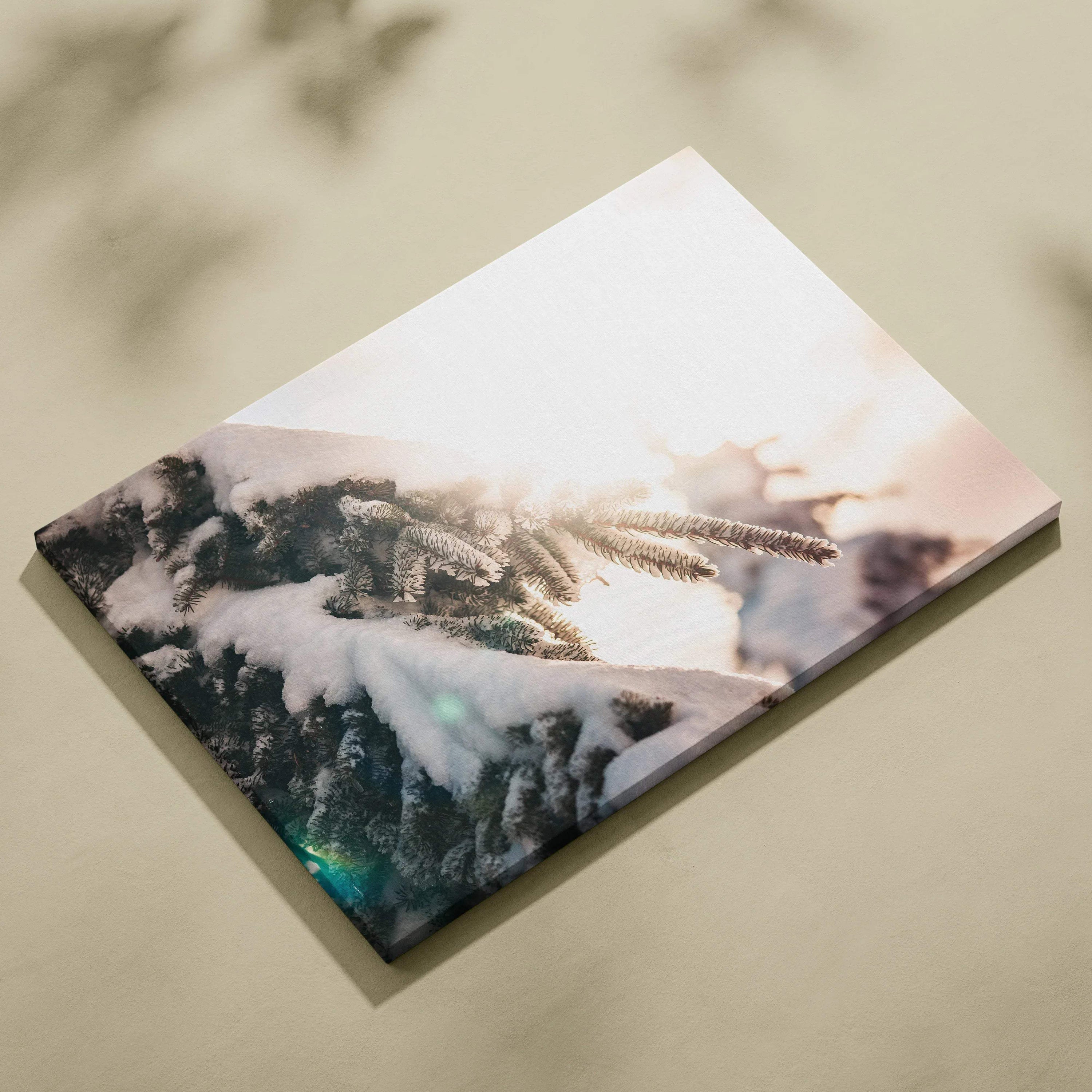 Canvas wall art featuring close-up of snow-covered evergreen branches with soft sunlight glow.