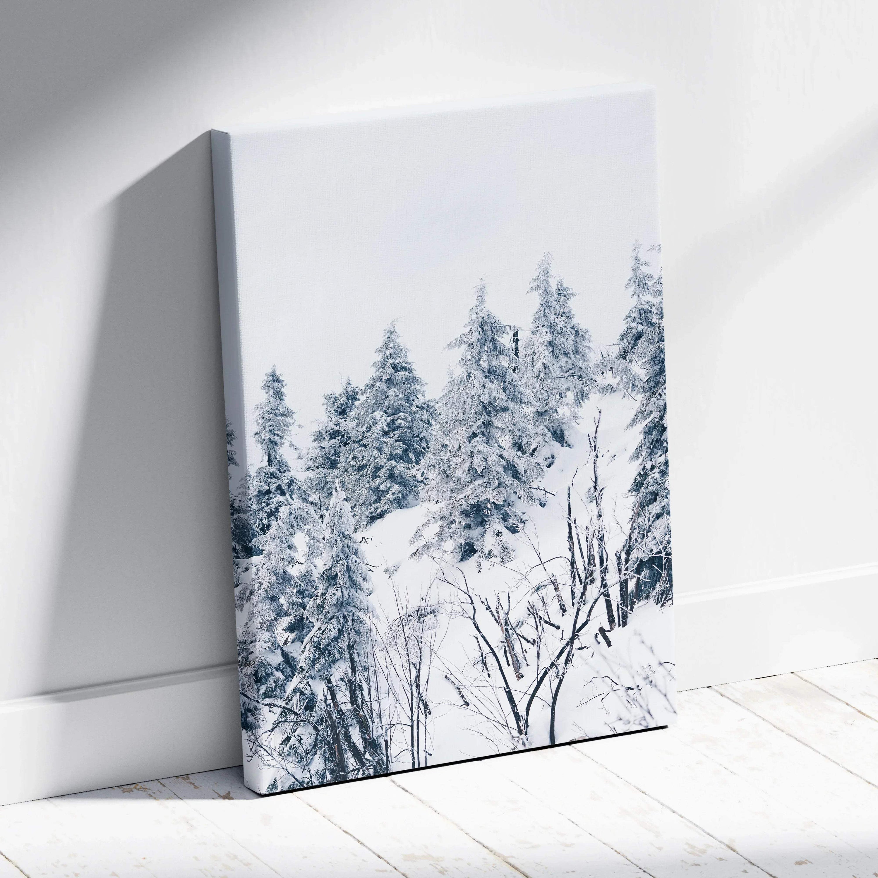 Canvas wall art featuring a snowy winter landscape with frosted pine trees and bare branches in soft blue and white tones.