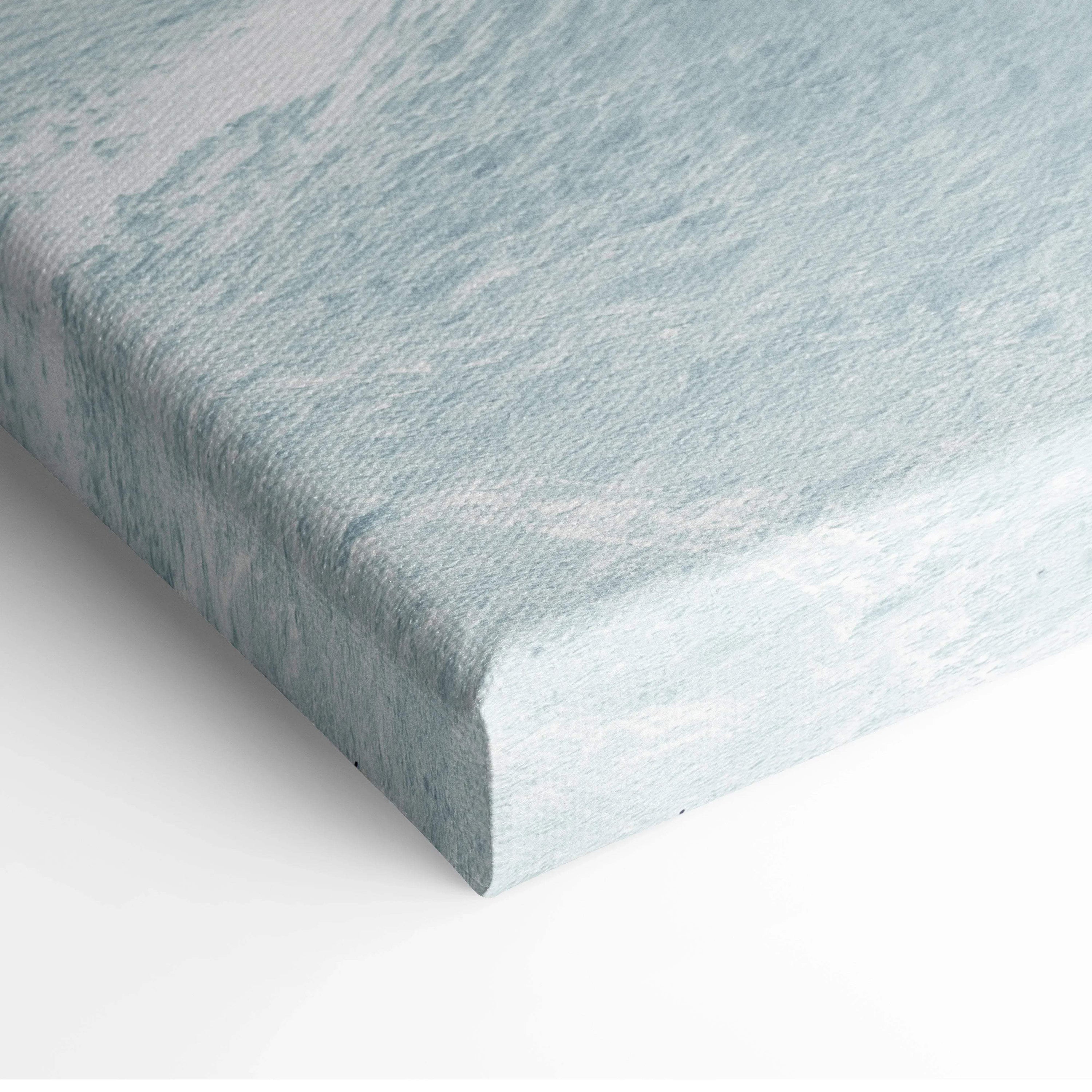 Corner of stretched canvas wall art with textured surface in soft blue and white tones.