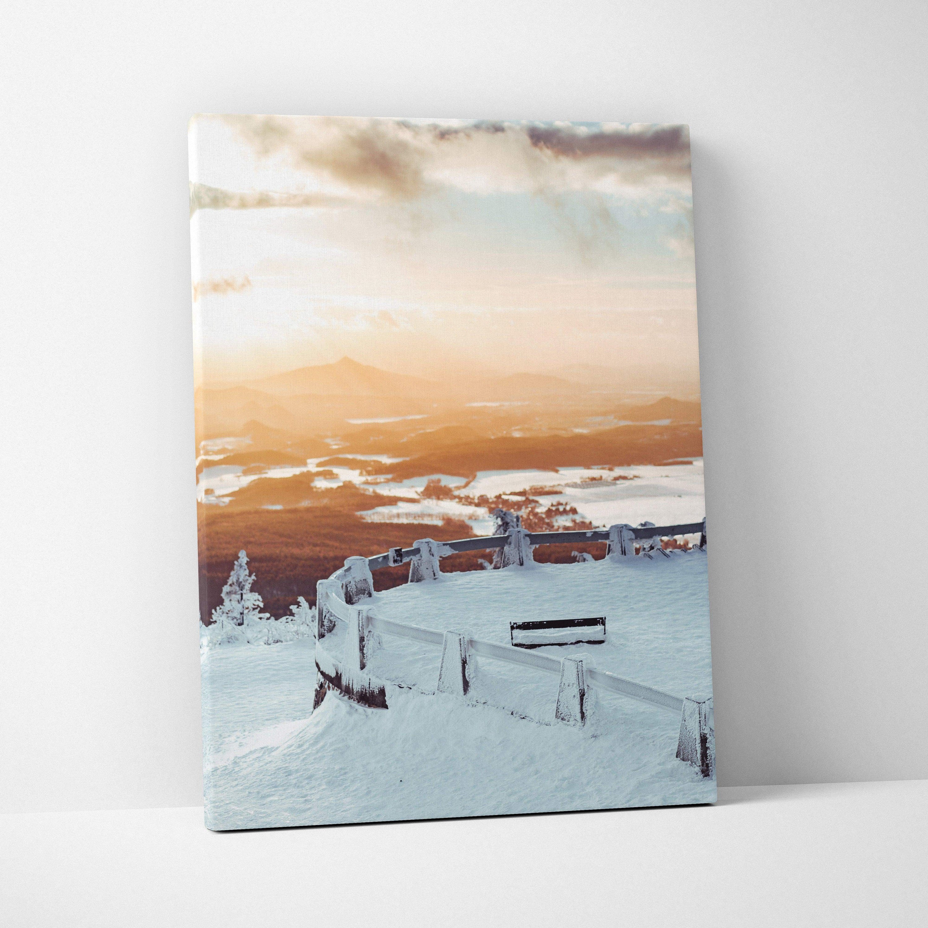 Canvas wall art featuring a snowy winter landscape at sunset with soft orange and blue sky tones over snow-covered trees and