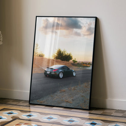 Nissan 350z poster wall art featuring a sleek black sports car on a scenic road at sunset.