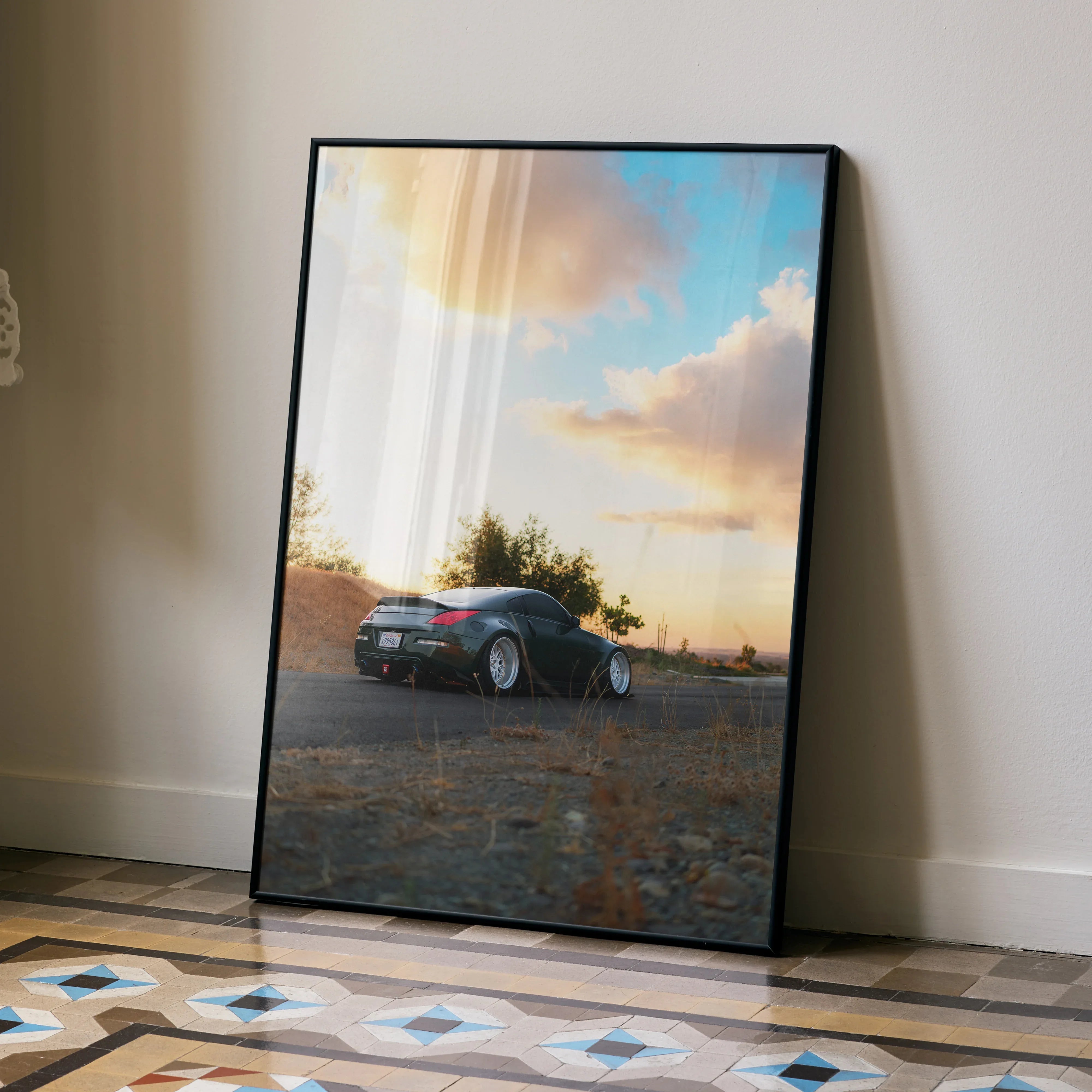 Nissan 350z car poster wall art with sunset sky in sleek black frame leaning on floor.
