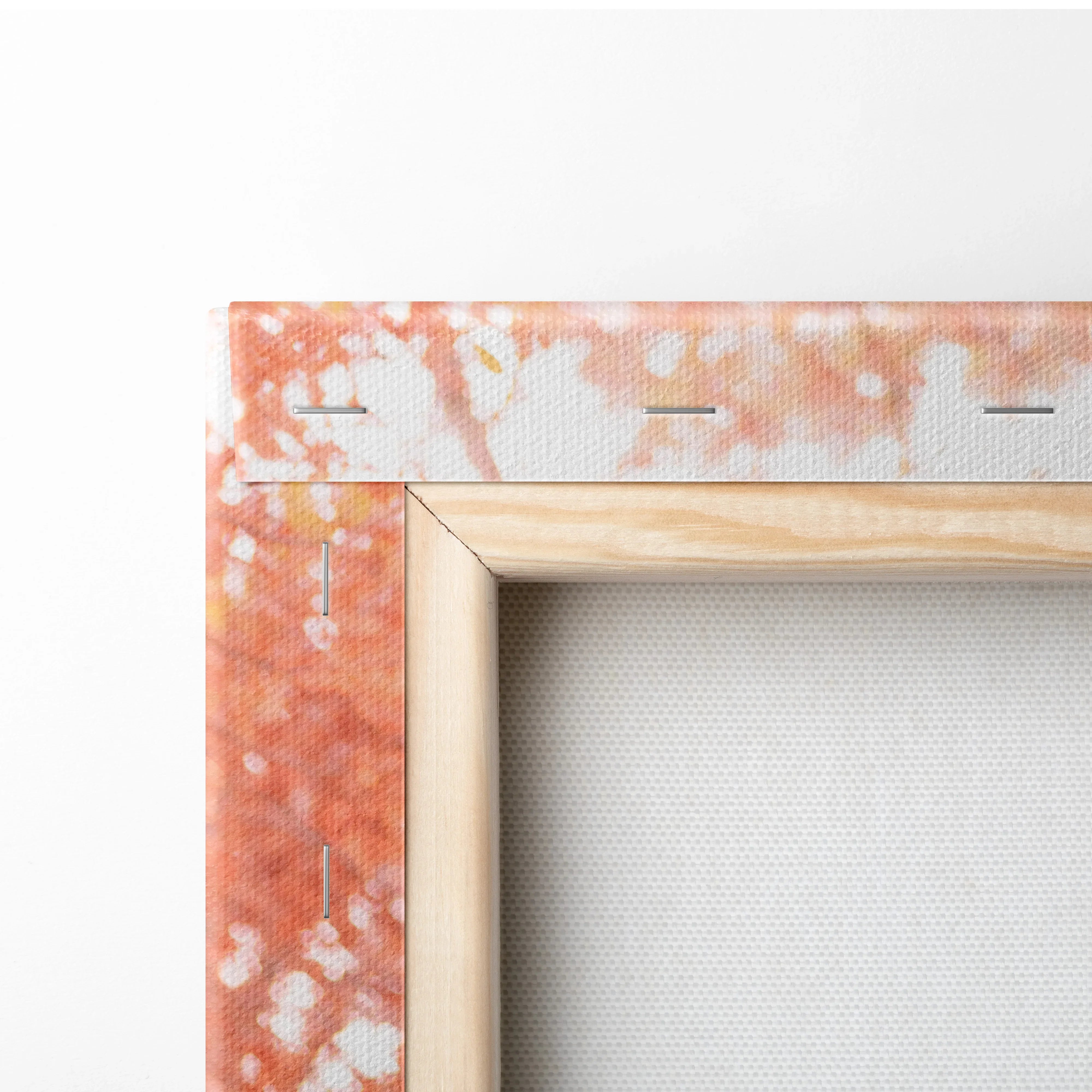 Close-up of wooden frame and orange abstract paint detail on canvas wall art with visible staples.