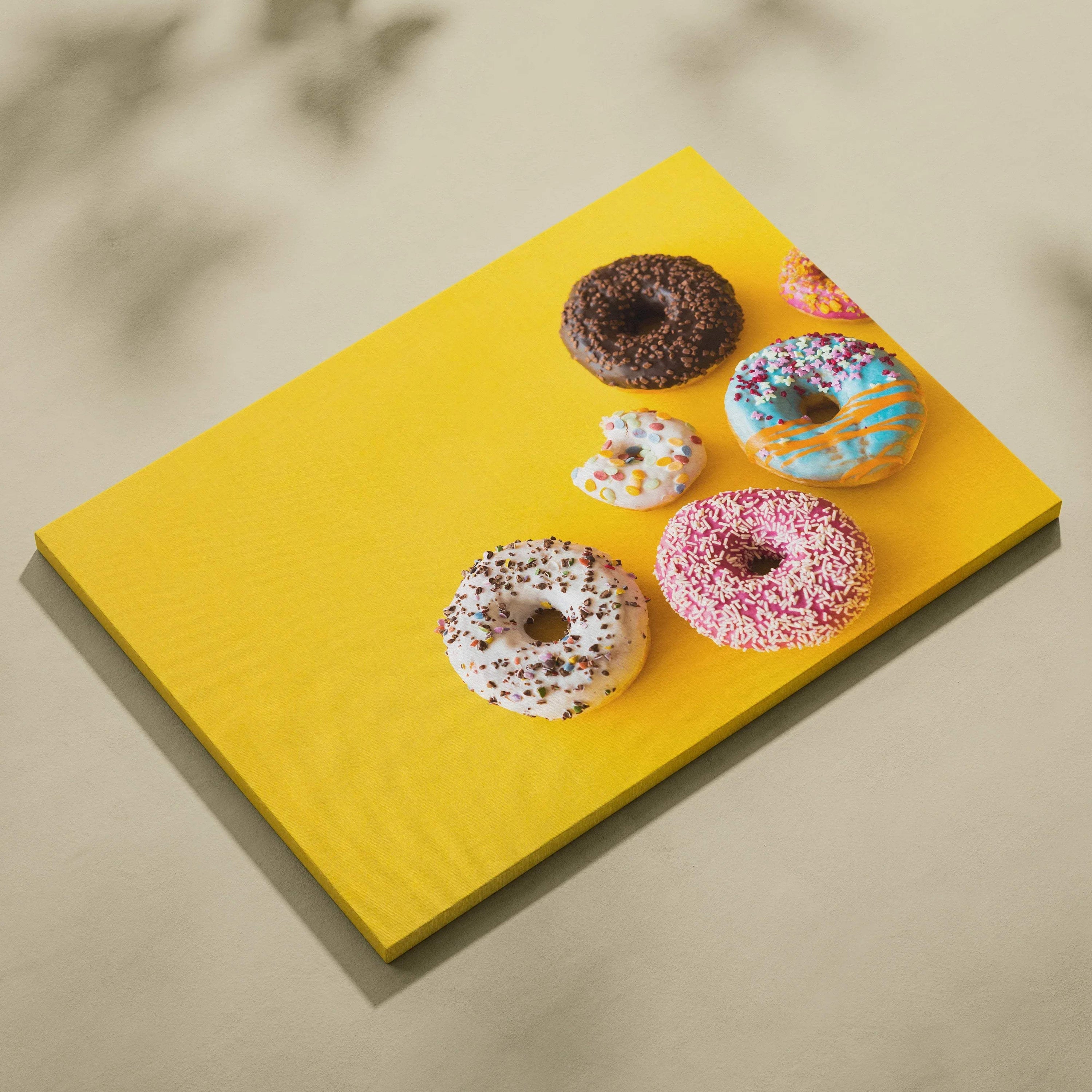 Canvas wall art featuring vibrant donuts with colorful glazes and sprinkles on a bright yellow background.