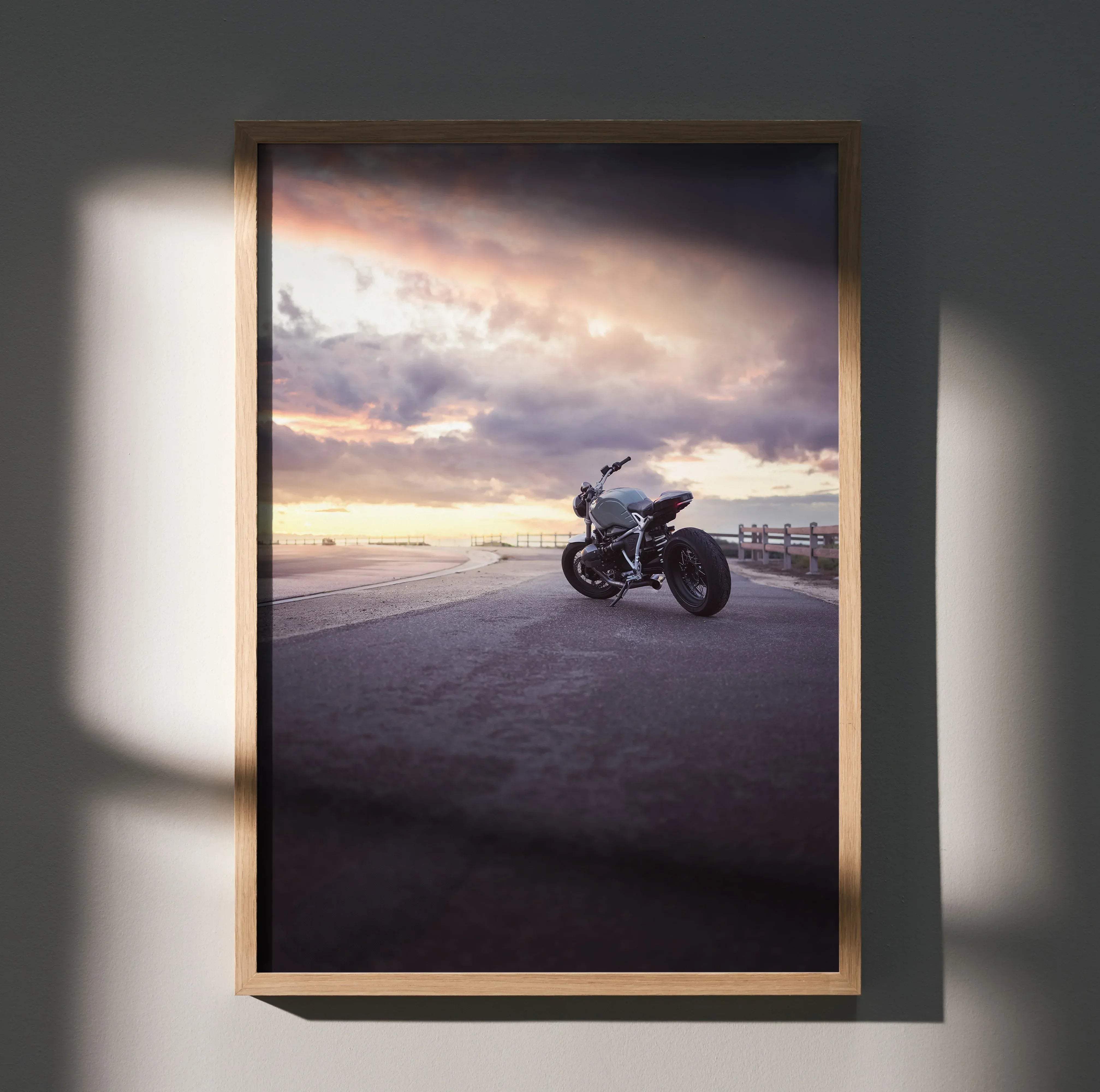 A framed BMW inspired r nine t silver motorcycle art print showing a coastal road at sunset with warm dramatic lighting