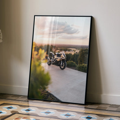 BMW S1000RR motorcycle poster leaning against wall with scenic sunset background and black frame wall art.