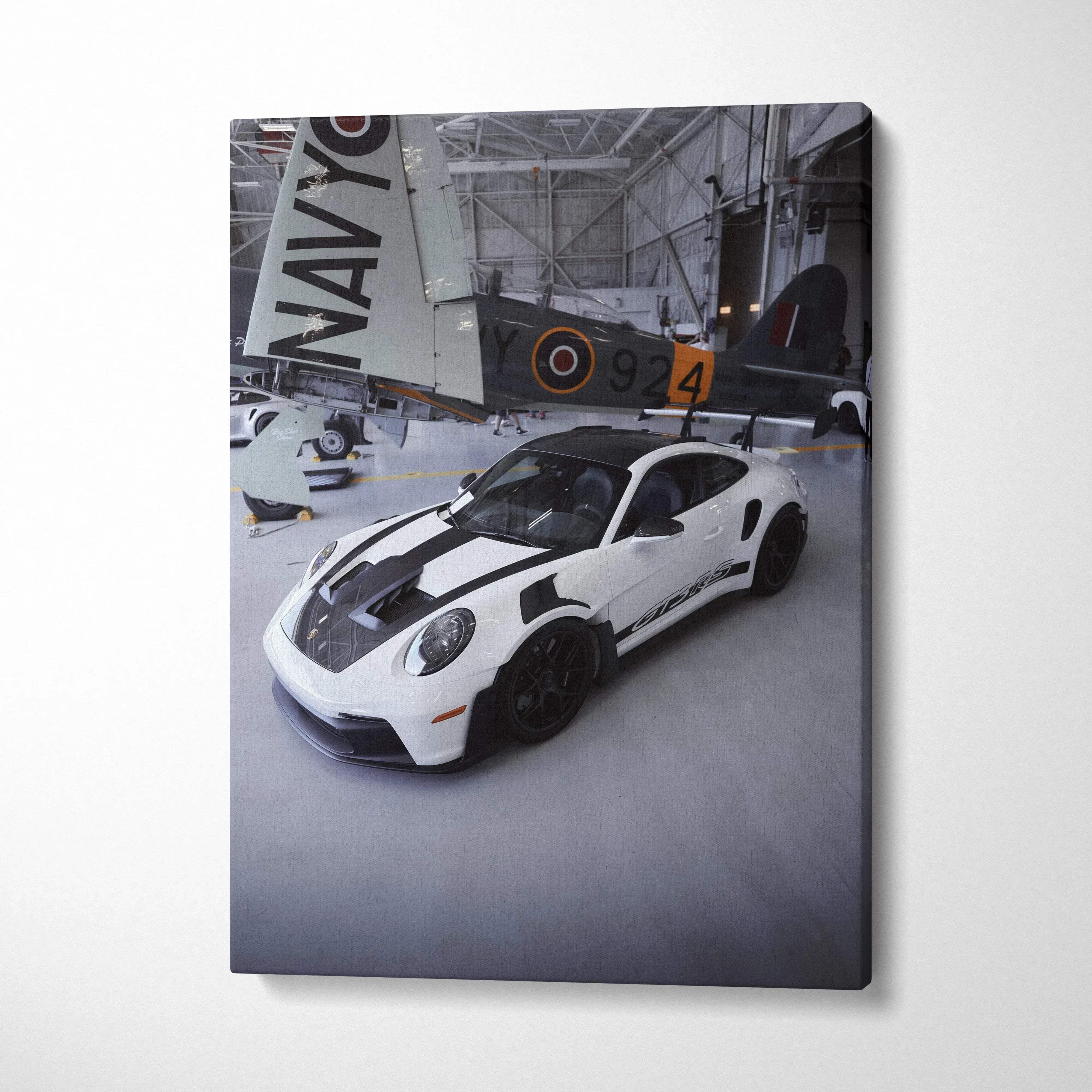 Vertical canvas art featuring a white Porsche 911 GT3RS with black stripes in an aviation hangar wall art piece.