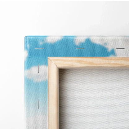 Close-up of canvas wall art corner with wooden frame and blue sky with white clouds print on textured fabric.