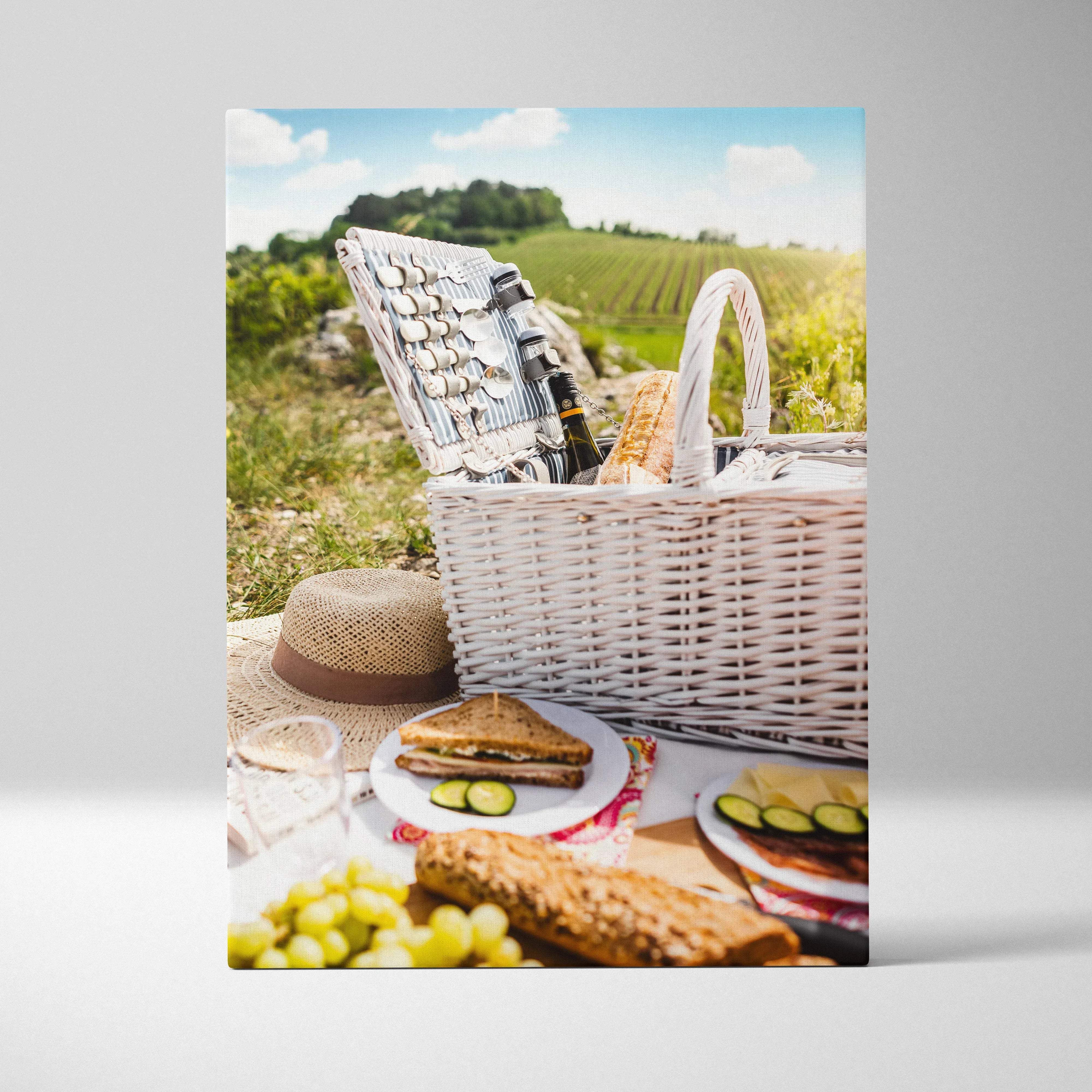 Rustic picnic scene canvas wall art featuring a white woven wicker basket with striped interior holding bread wine and cutlery