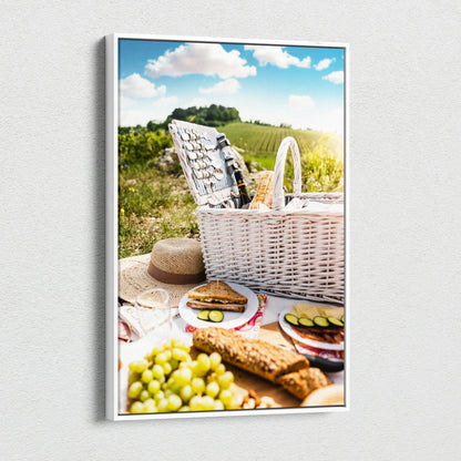 Vertical canvas wall art showing a picnic scene with white wicker basket, grapes, bread, and countryside decor.
