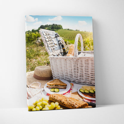 Vibrant canvas wall art featuring a sunny outdoor picnic scene with a white wicker basket, sandwiches, grapes, and cucumber.