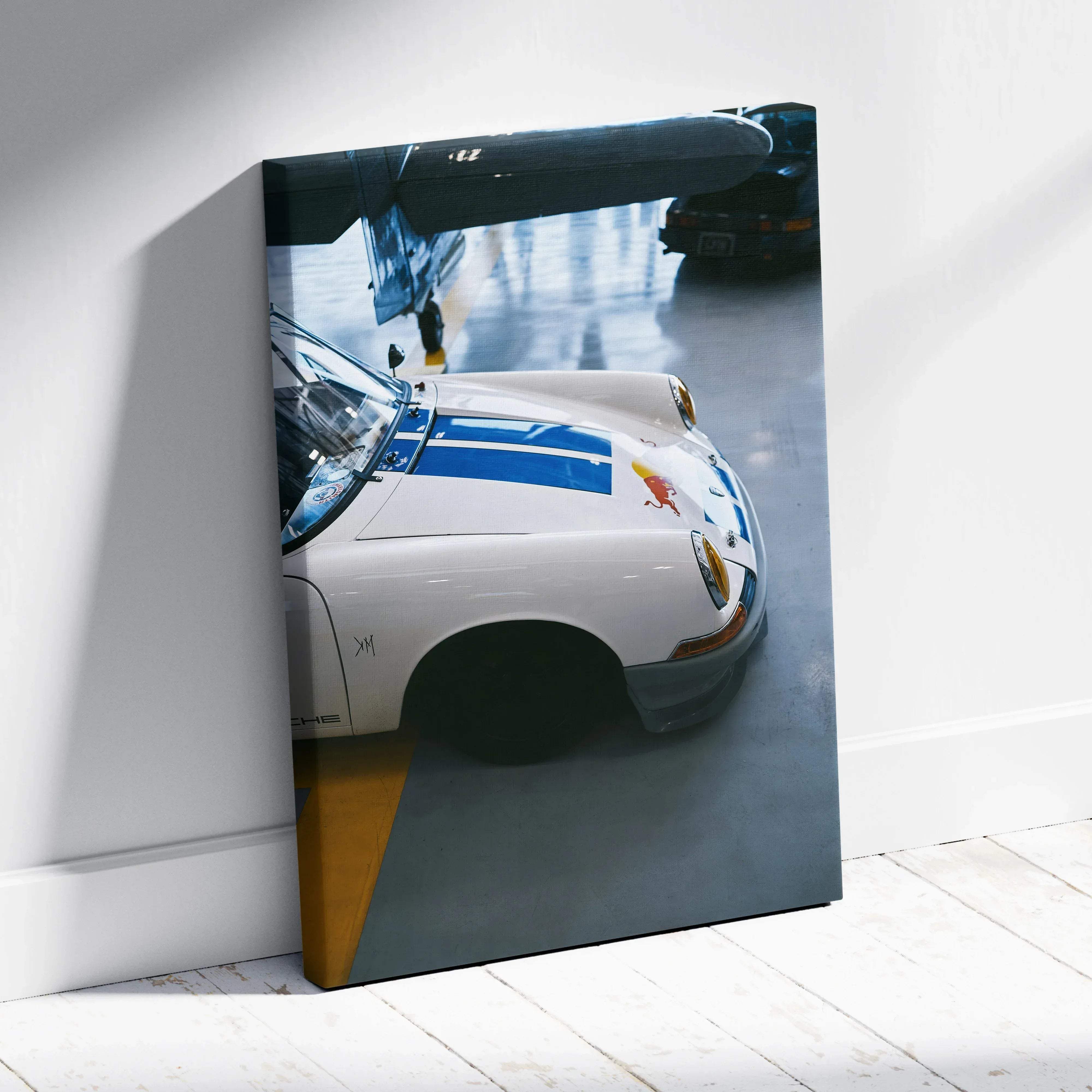 Canvas wall art featuring a white Porsche 911 with blue racing stripes and a red bull logo leaning against a wall