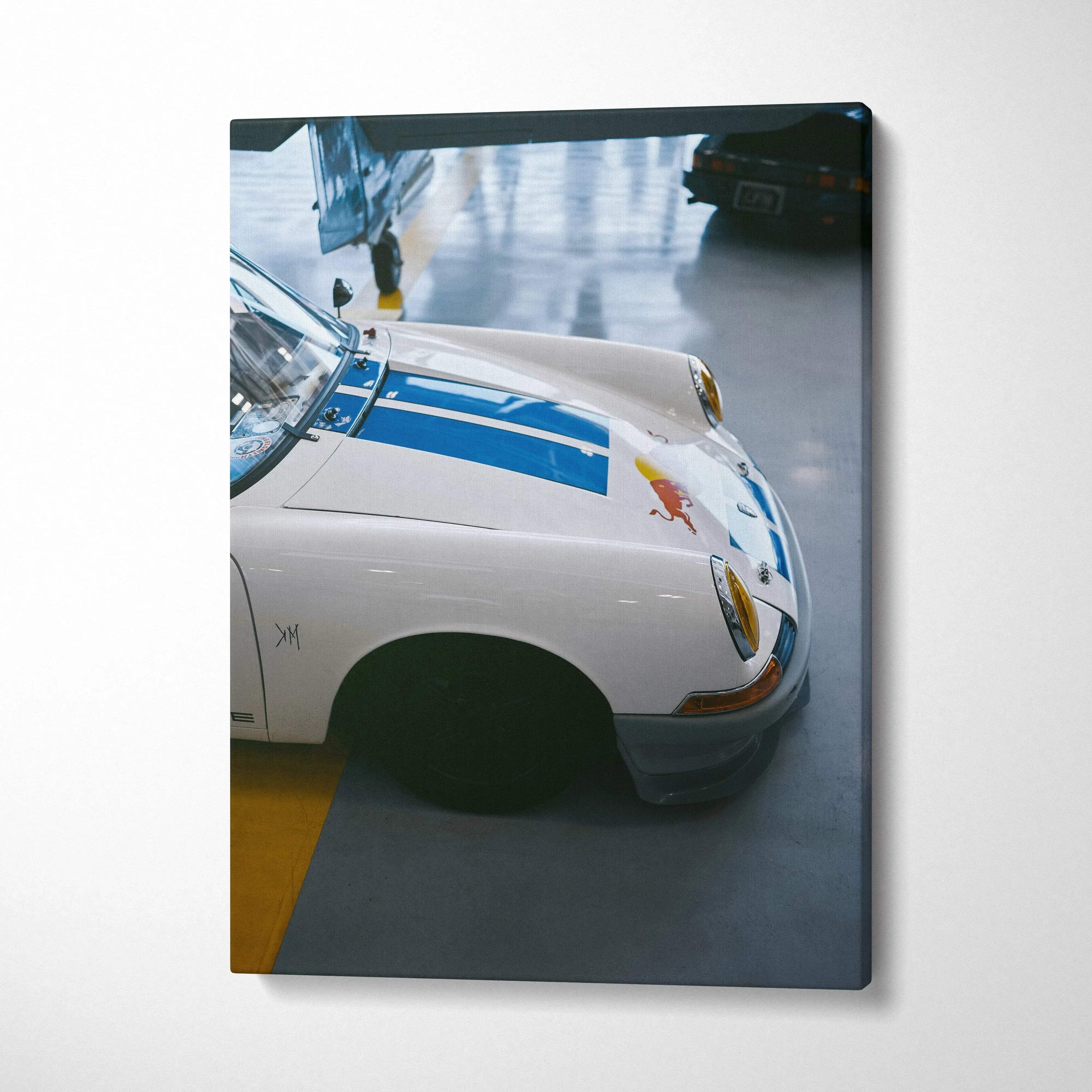 Vertical canvas wall art featuring a close-up of a white Porsche 911 with blue racing stripes in a garage setting.