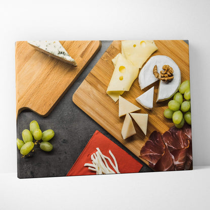 Canvas wall art featuring a rustic lunch table with assorted cheeses, walnuts, green grapes, and cured meats on wooden.