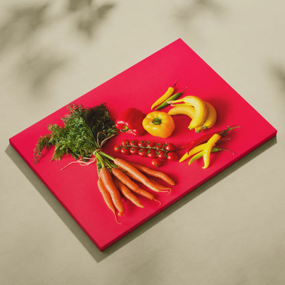 Bright red canvas wall art featuring realistic bananas, yellow and orange peppers, cherry tomatoes, and fresh carrots.