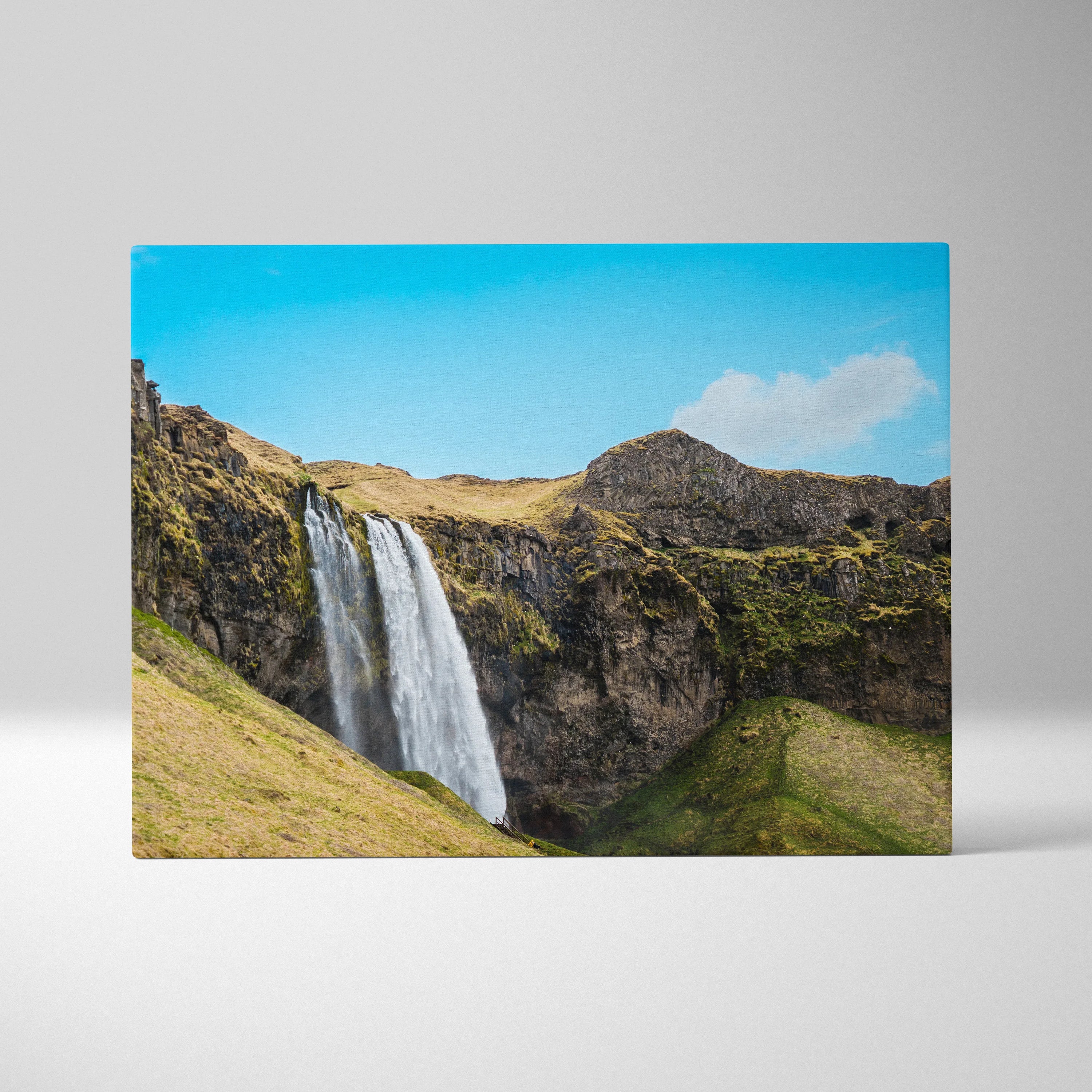 Canvas wall art featuring a vibrant Icelandic waterfall cascading over rocky cliffs under a bright blue sky.