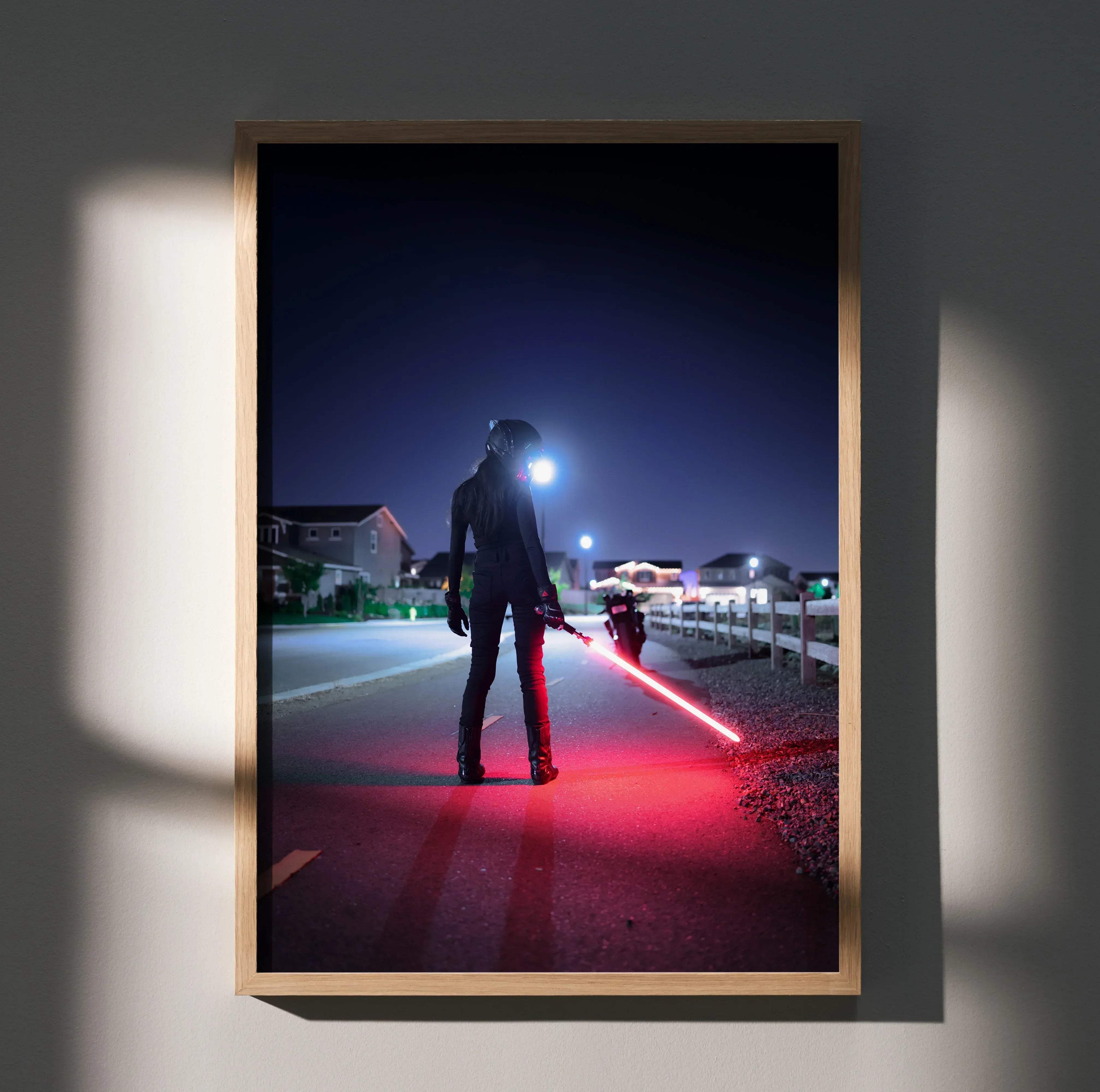 A framed biker poster featuring a female in black gear with a glowing red lightsaber on a nighttime street