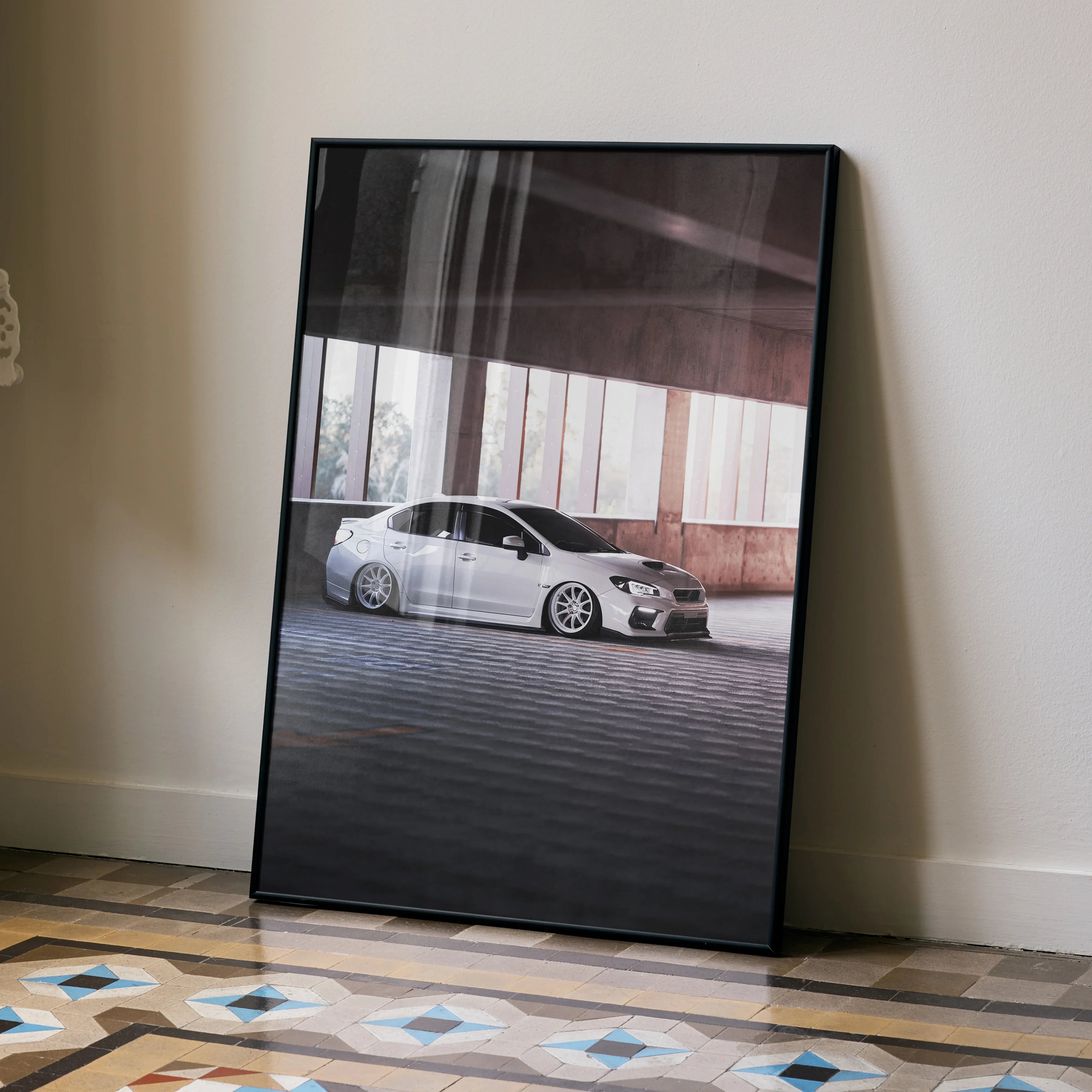 Subaru WRX white car poster wall art leaning against beige wall with patterned tile floor.