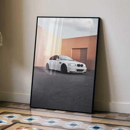 BMW E46 M3 performance poster in black frame leaning against beige wall with geometric tiled floor, automotive wall art.