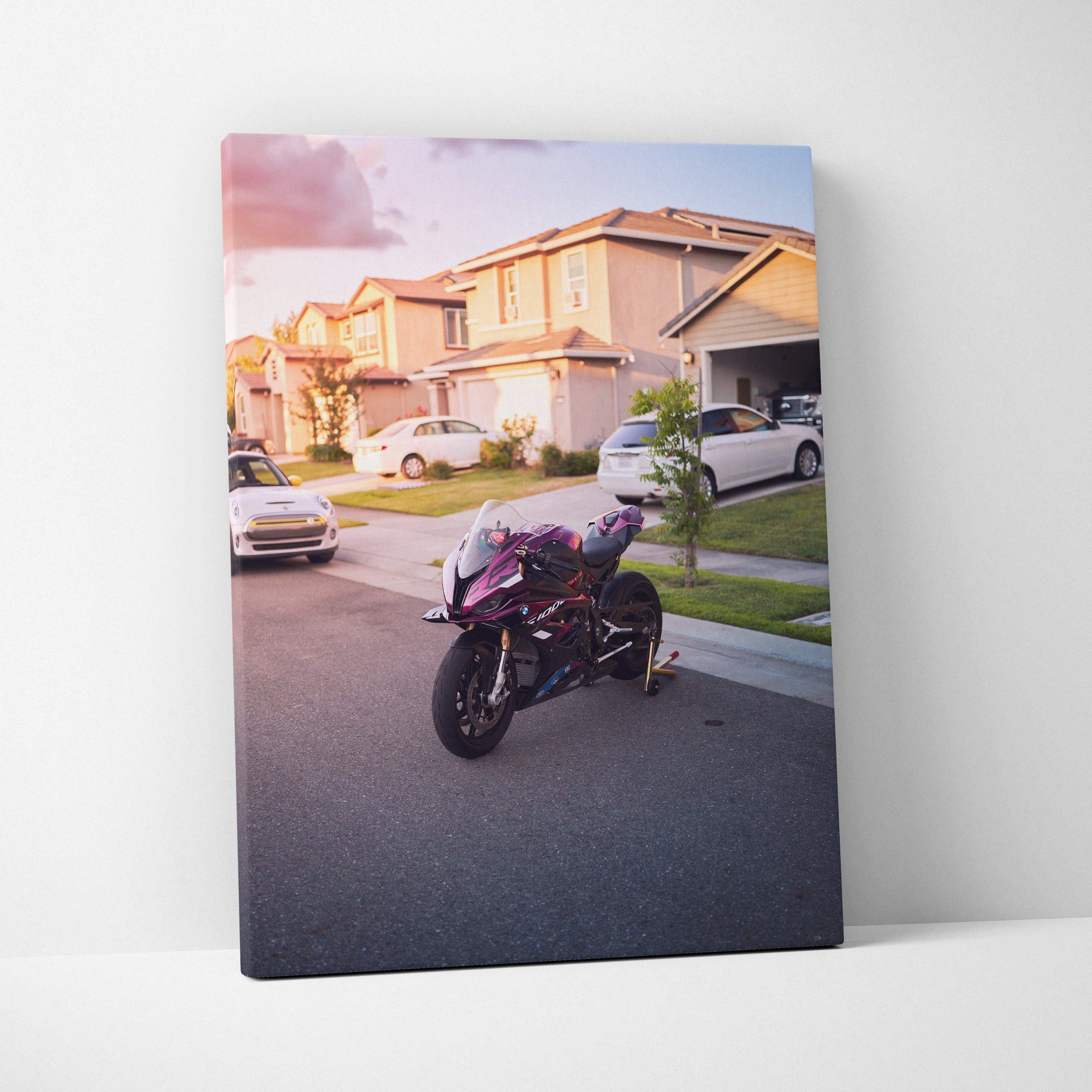 Vertical canvas wall art featuring a BMW S1000RR motorcycle parked in a suburban neighborhood at sunset.