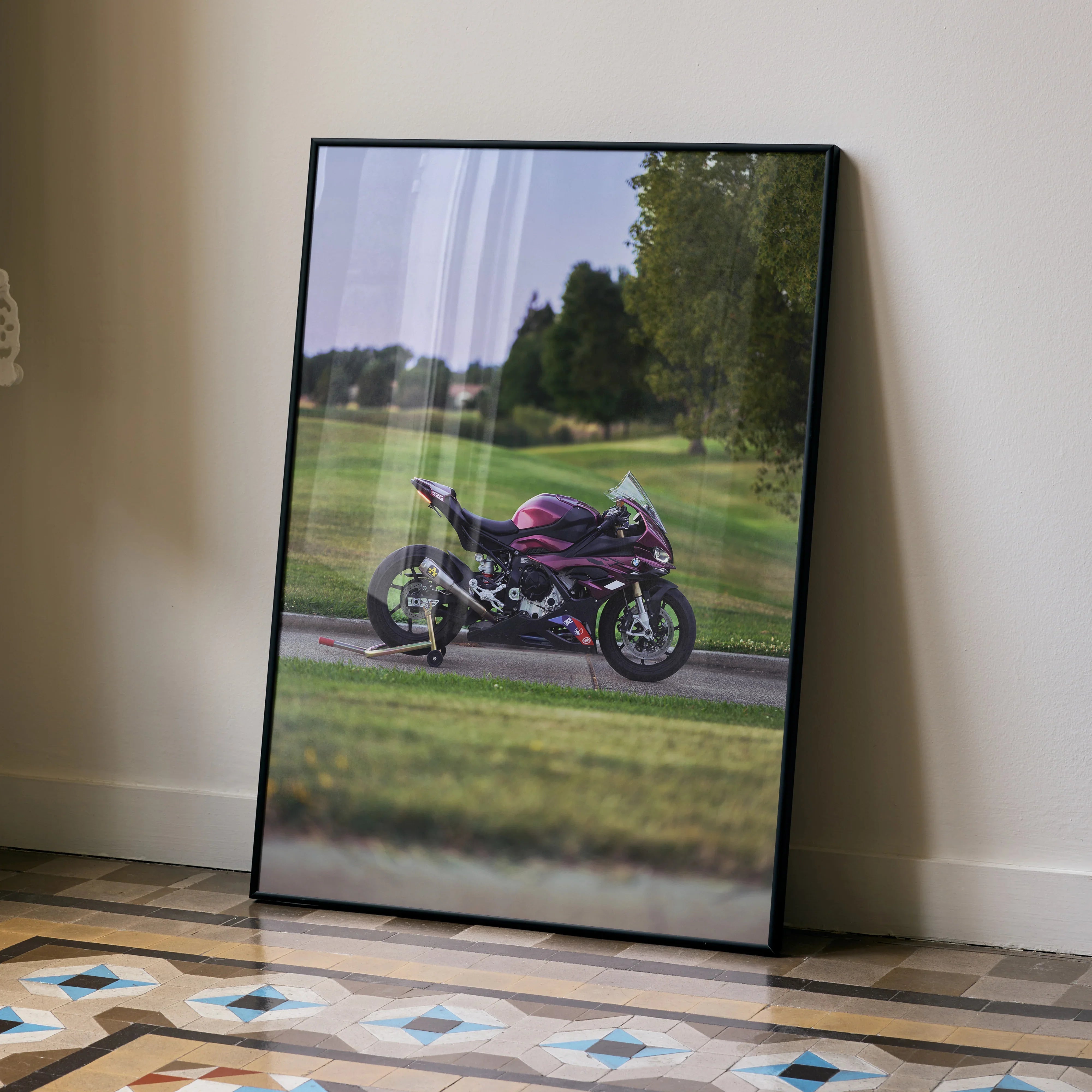 BMW S1000RR motorcycle poster with purple bike on racetrack, framed wall art leaning against beige wall.