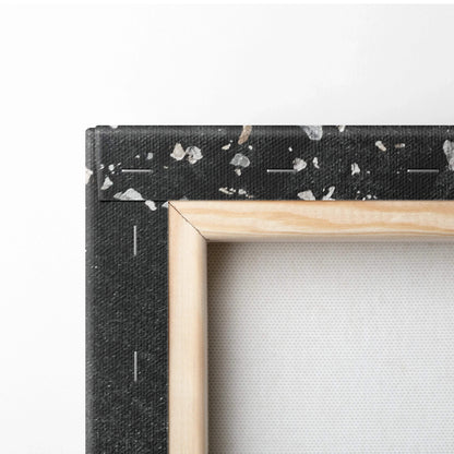 Close-up of stretched canvas with natural wood frame and black edge featuring white abstract speckles.