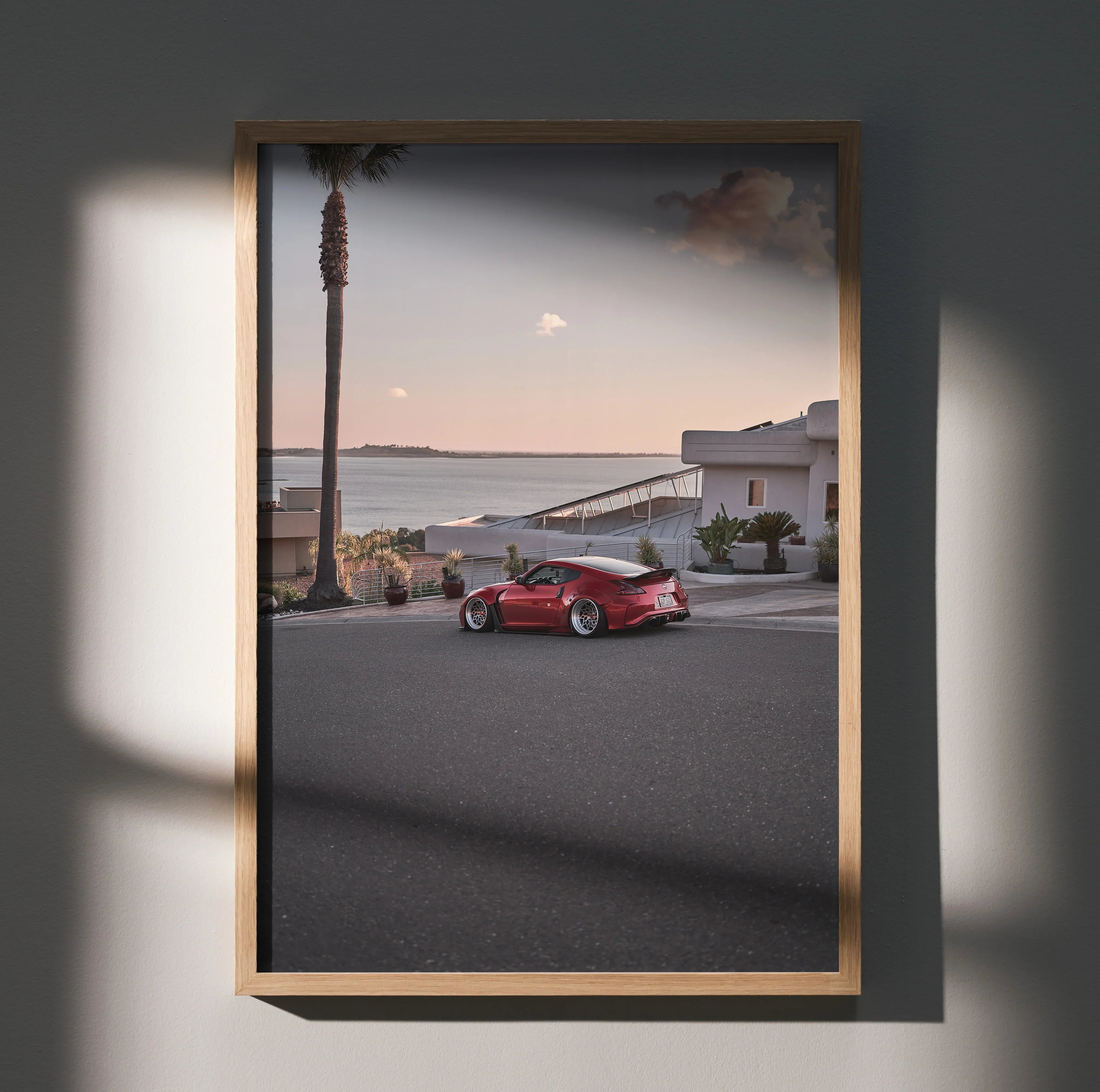 Nissan 370z red sports car on coastal road at sunset poster wall art in wooden frame.