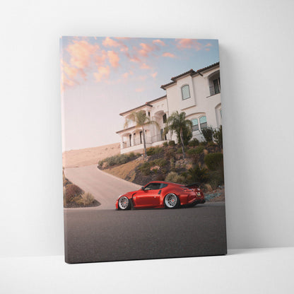 Red Nissan 370z sports car parked by hillside mansion at sunset on vertical canvas wall art.