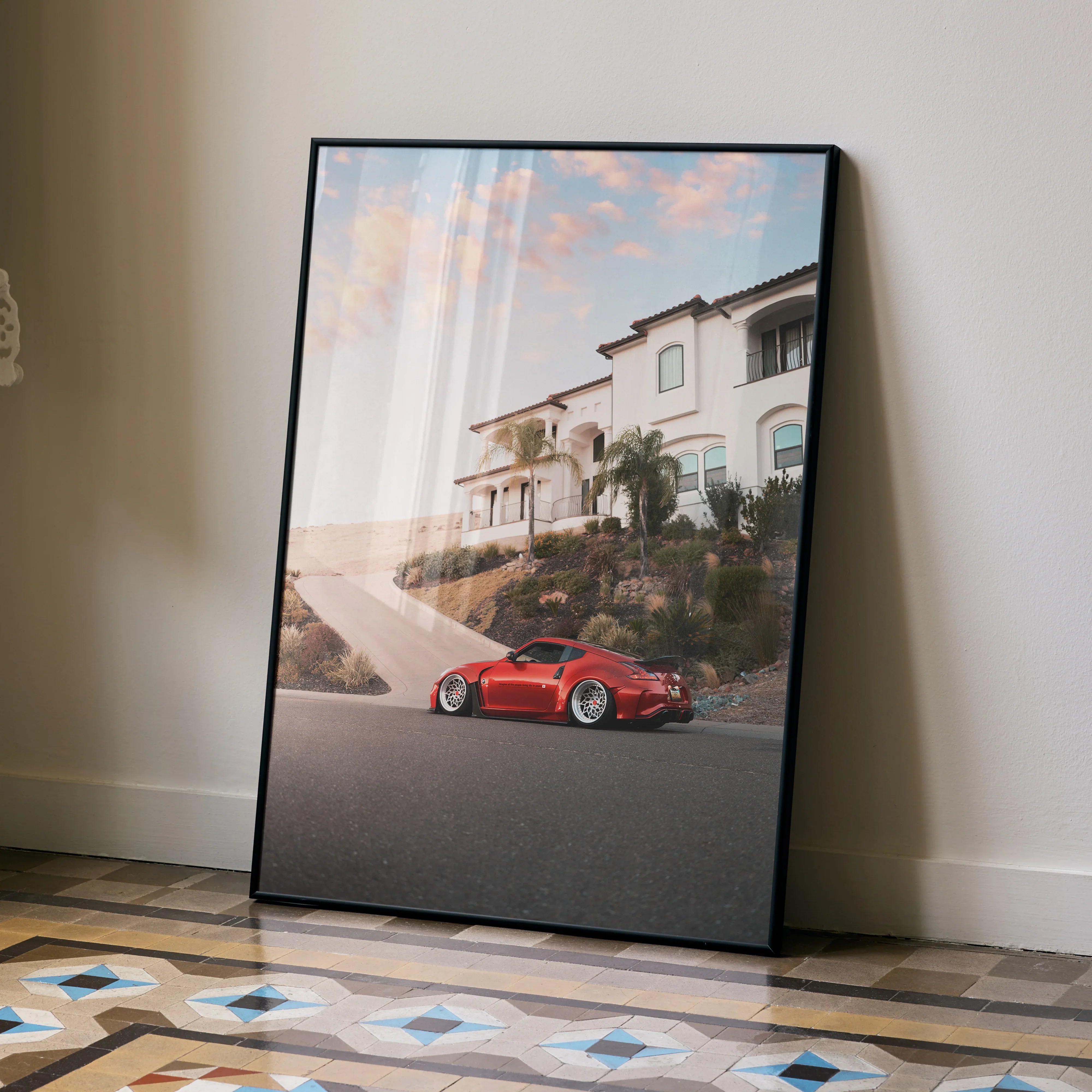 Red Nissan 370z parked by a white house at sunset poster wall art in black frame.