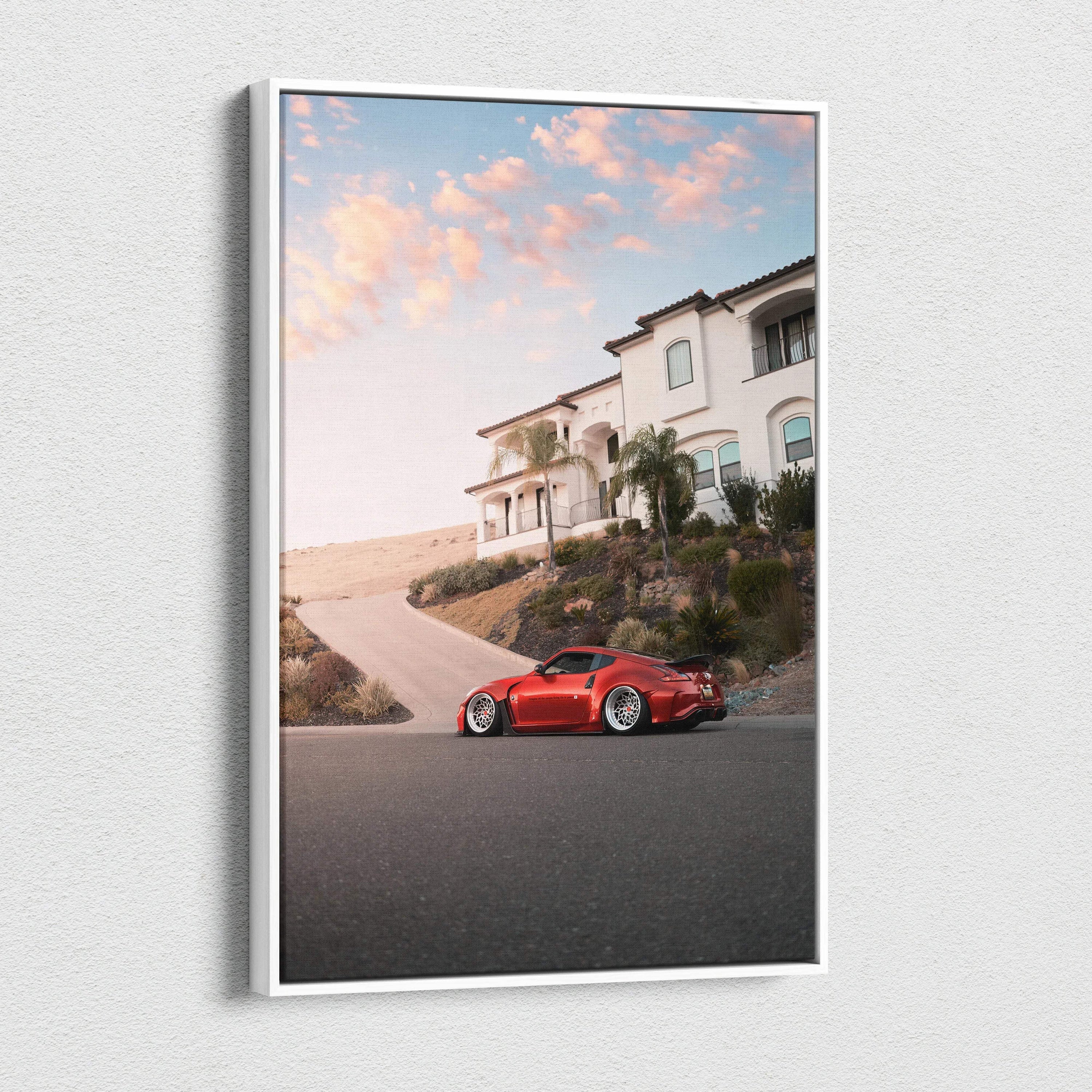 Vertical canvas wall art featuring a red Nissan 370z parked by a hillside house under a pink sunset sky.