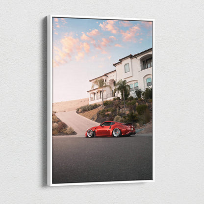 Vertical canvas wall art featuring a red Nissan 370z parked by a hillside house under a pink sunset sky.