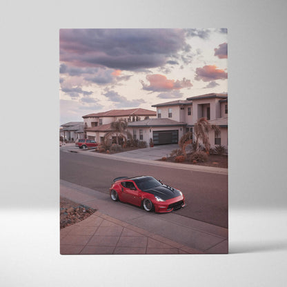 Vertical canvas wall art featuring a red Nissan 370z parked in a suburban neighborhood at sunset with dramatic clouds.
