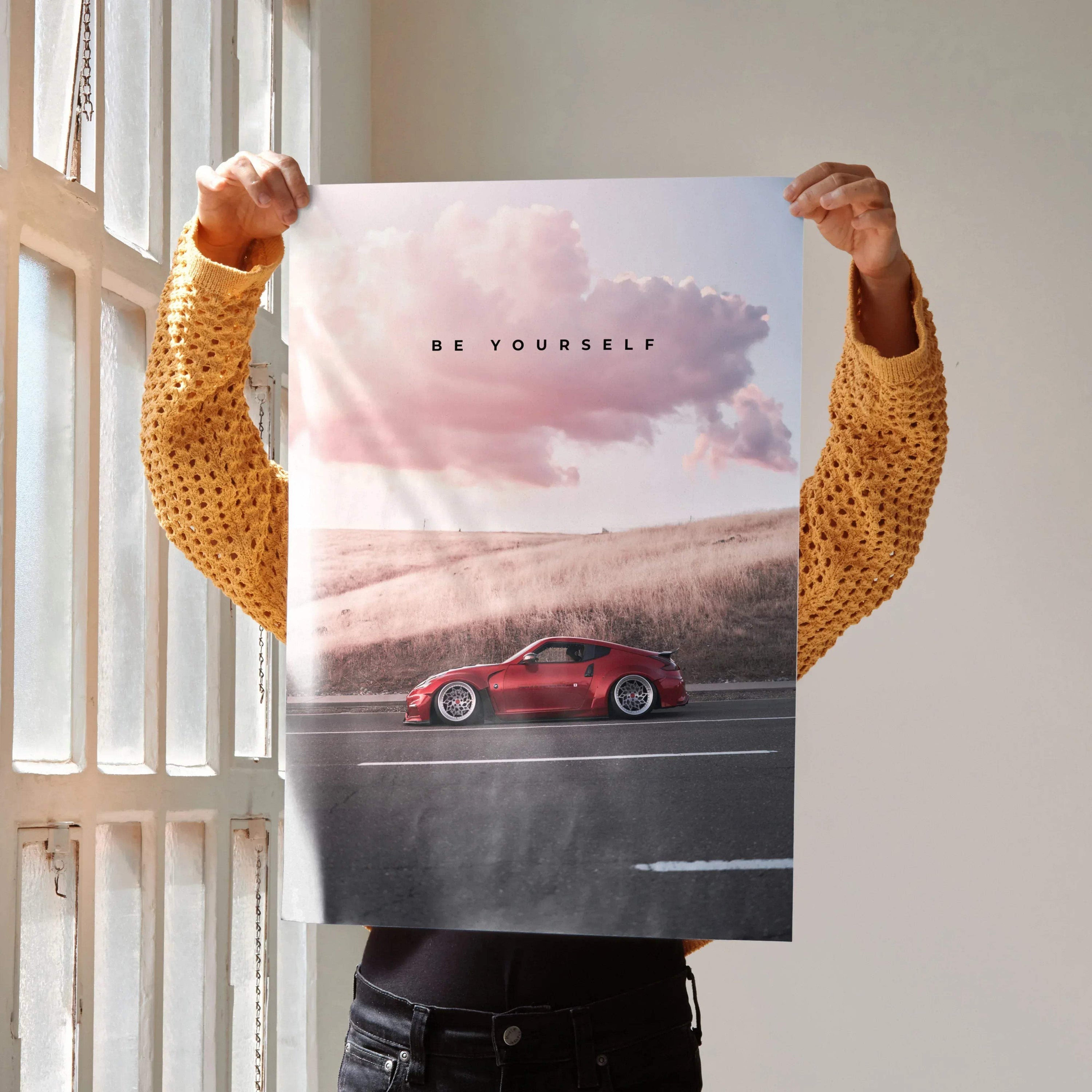 Motivational poster wall art with red Nissan 370z racing on road under pink cloudy sky and "Be Yourself" text.