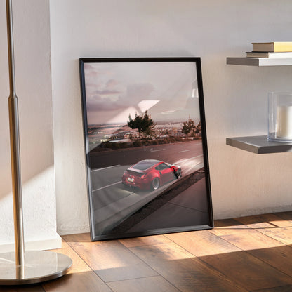 Nissan 370z red car driving on coastal road at sunset wall art poster in black frame.